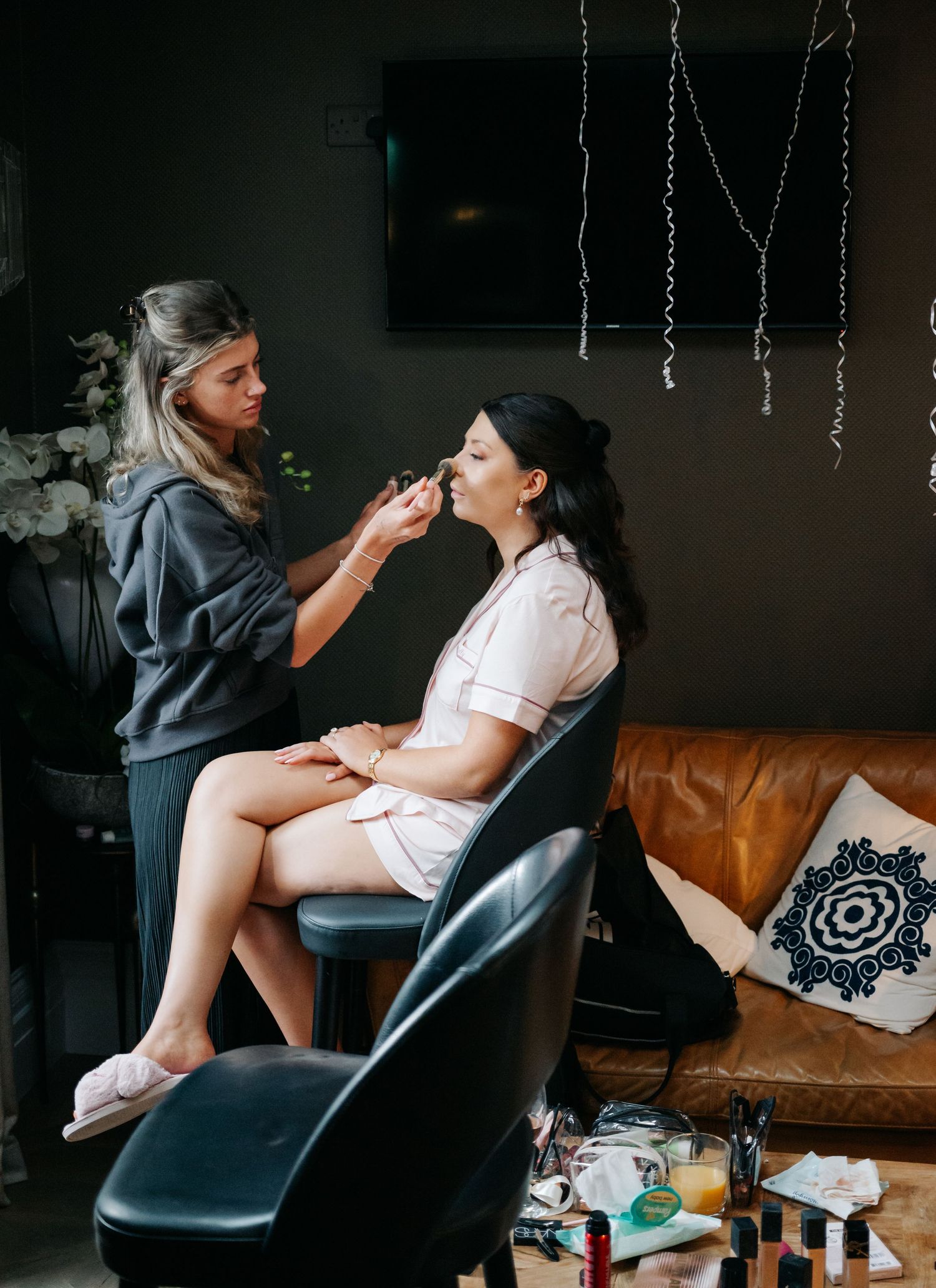 Makeup artist applies cosmetics to client in leather chair during wedding preparation.