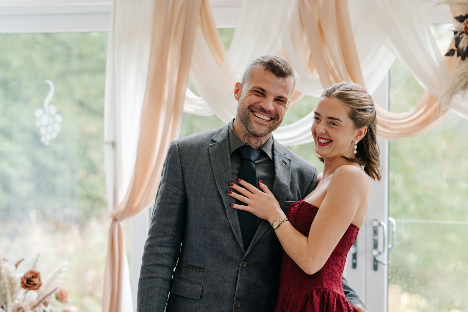 Couple sharing a joyful moment together during formal event with peach drapery in background.