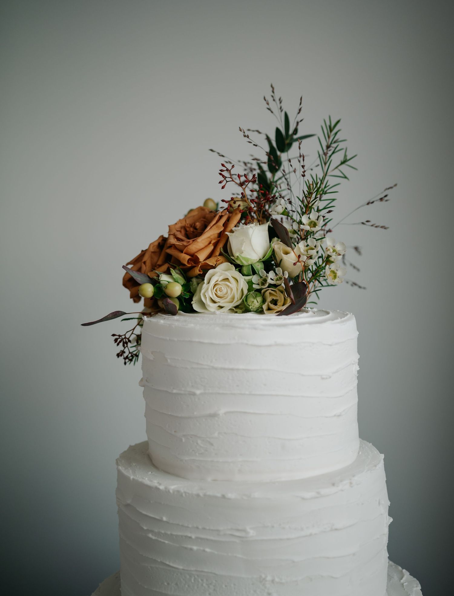 Close-up of a white wedding cake decorated with fresh roses and delicate floral accents.