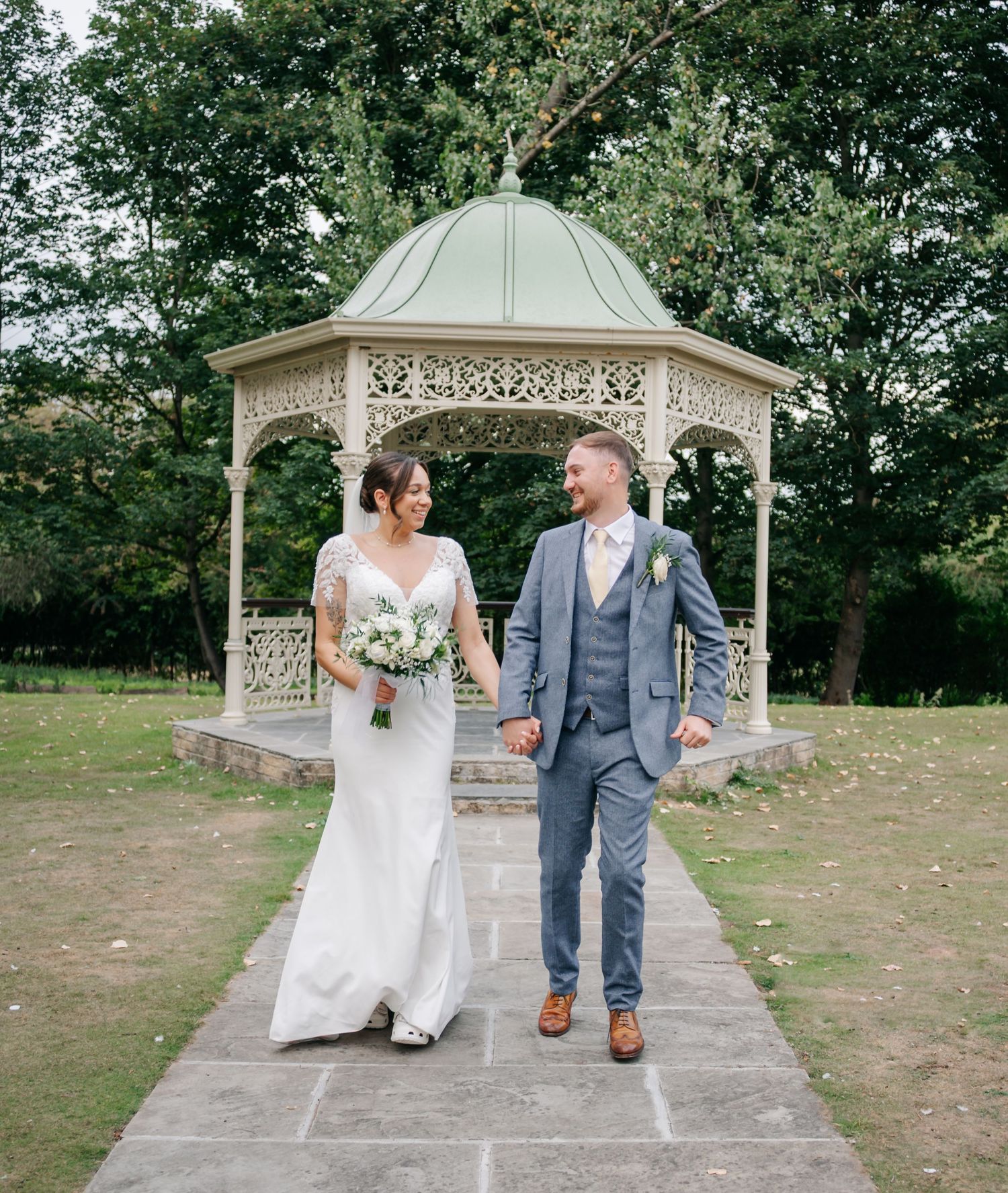 Wedding couple posing in front of an ornate white garden gazebo.