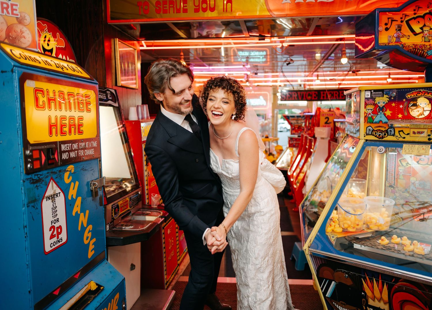 A couple shares a joyful moment together in a colorful arcade filled with vintage games and neon lights.