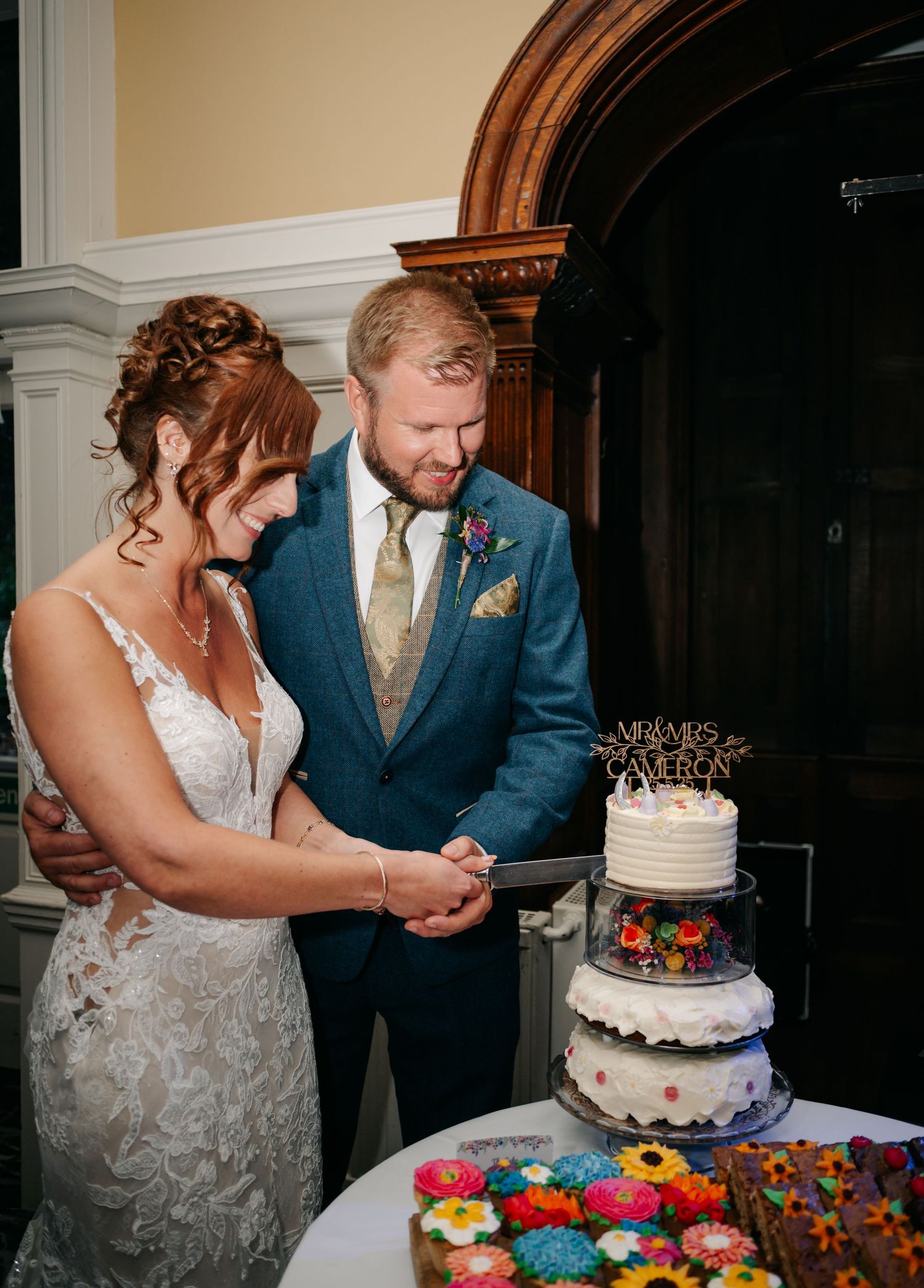 Couple cutting their three-tiered wedding cake decorated with colorful flowers.