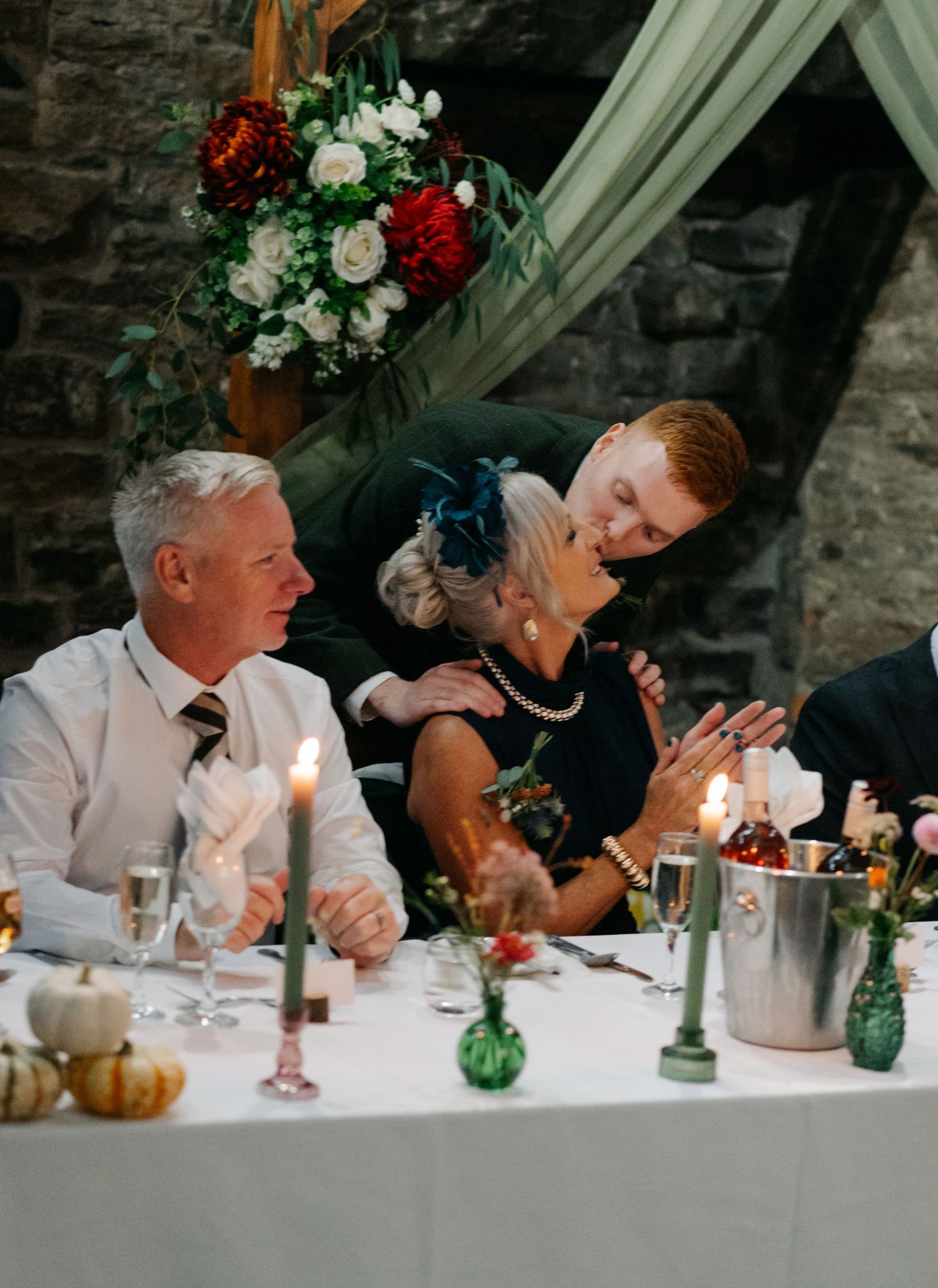 Wedding guests seated at long table with candlelit green glass decorations.