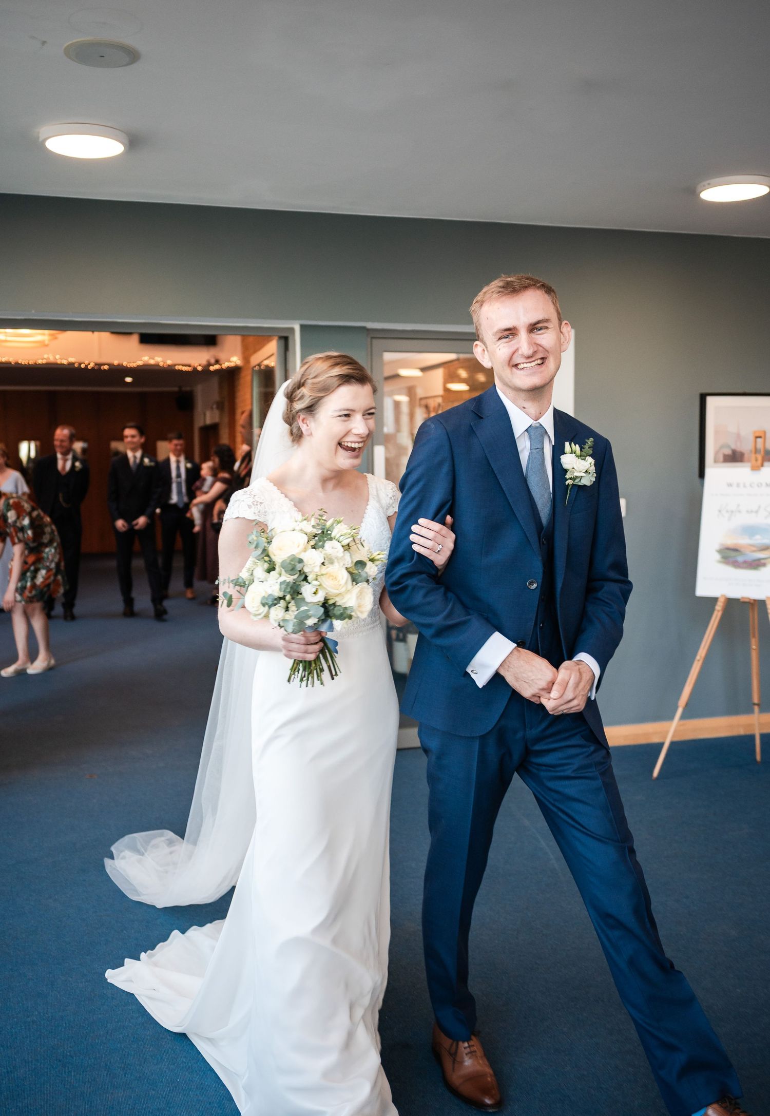 A wedding couple sharing a joyful moment in a modern venue hallway.