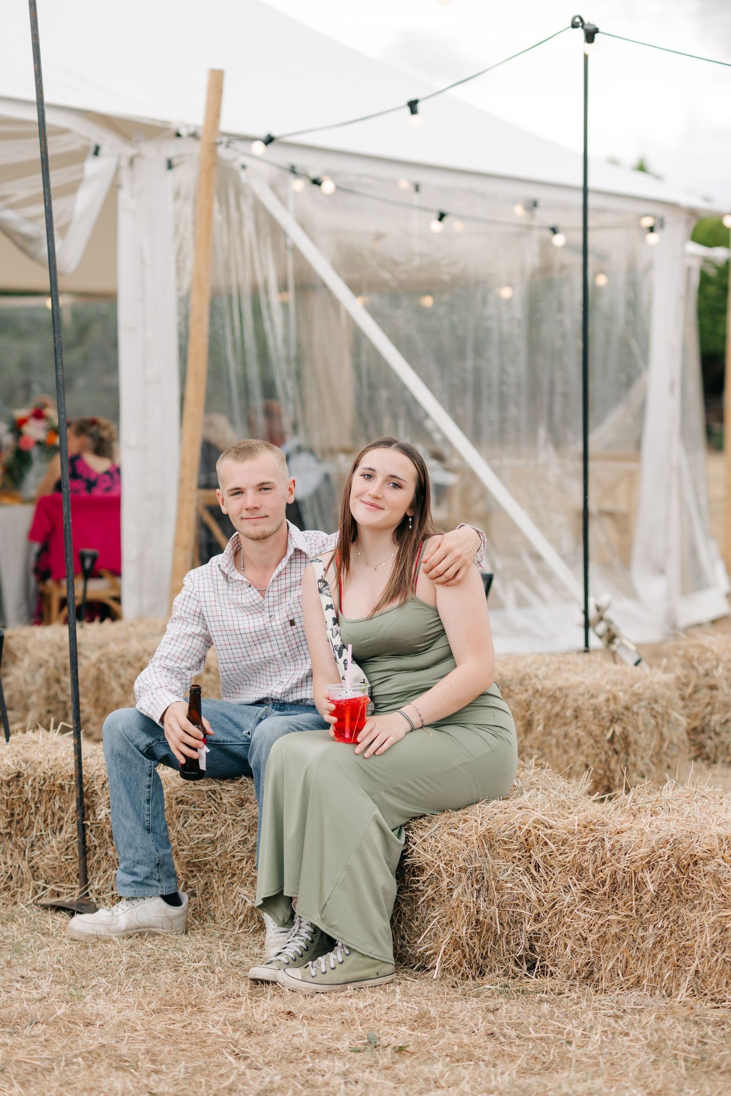 Rustic outdoor event setting with hay bale seating and string lights under a white tent.
