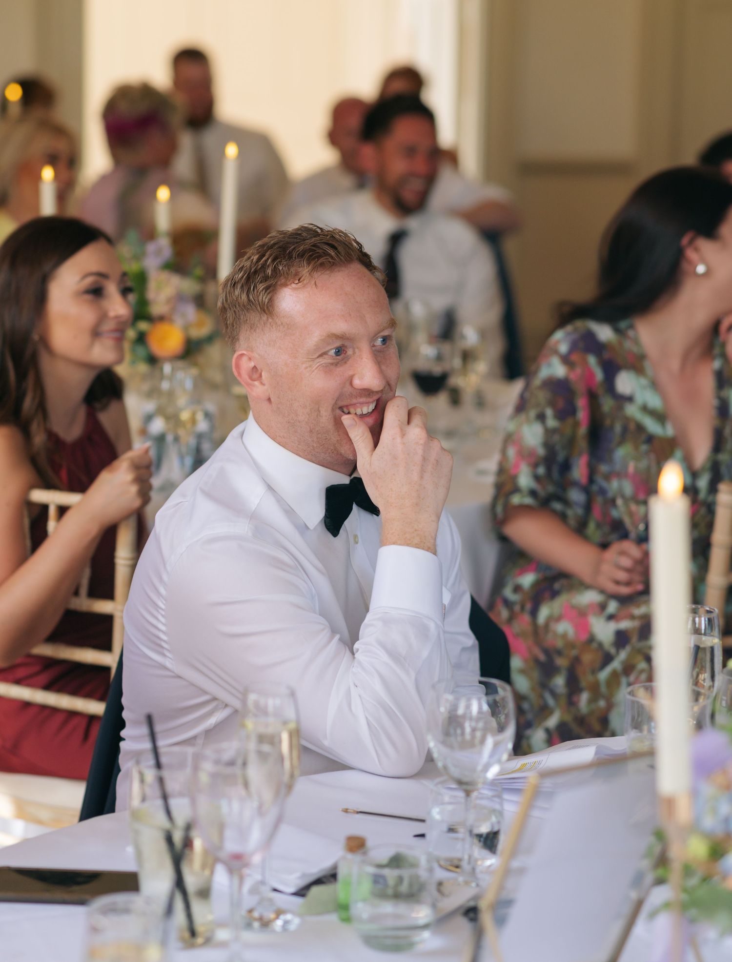Wedding guests seated at reception tables with floral centerpieces and candlelight.