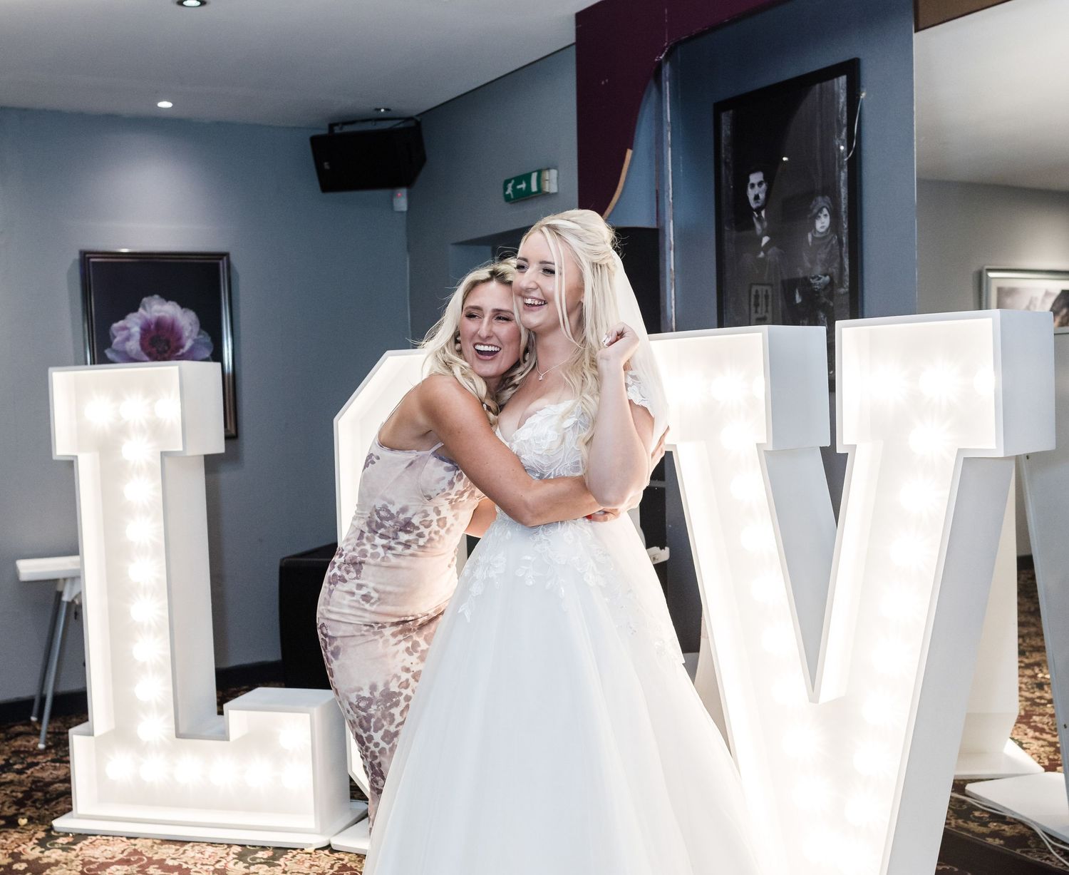Two people embrace joyfully in front of decorative LOVE letters at a wedding celebration.