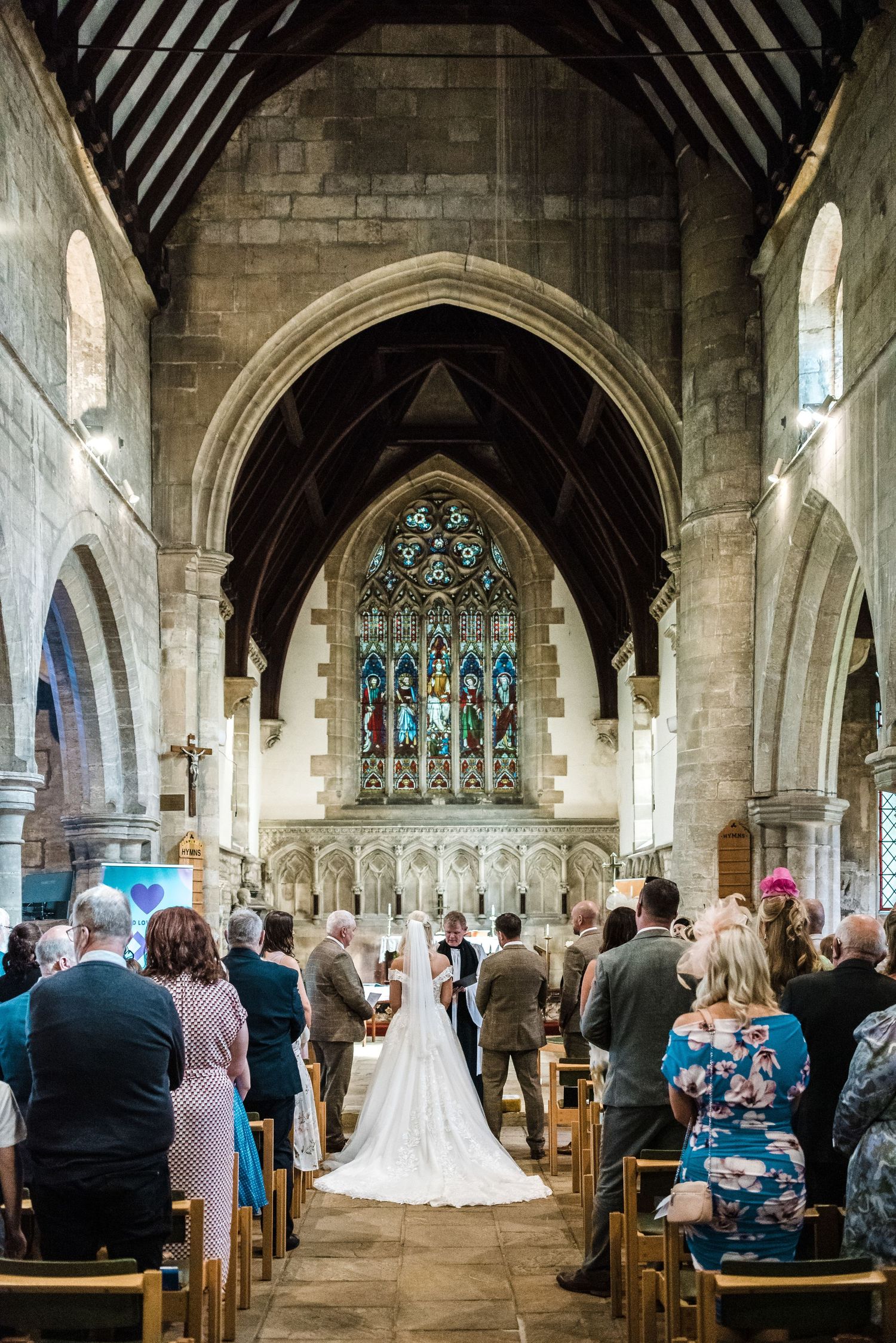 Wedding ceremony in grand stone church with stained glass windows and vaulted Gothic architecture.