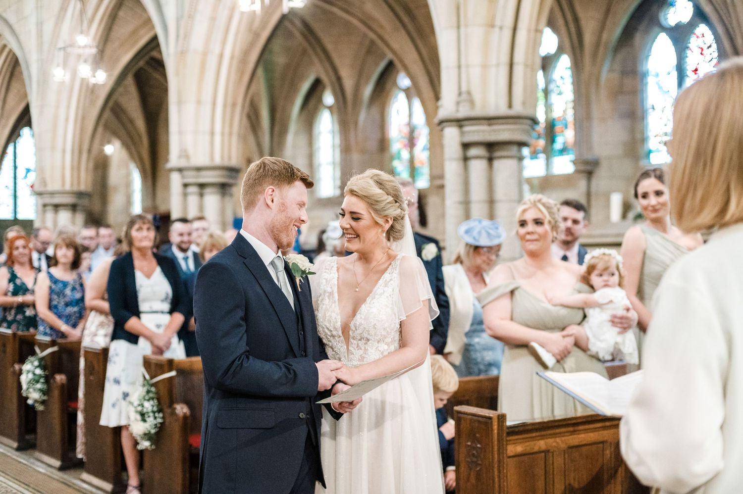 Wedding ceremony in progress inside a beautiful church with vaulted ceilings and arched windows.