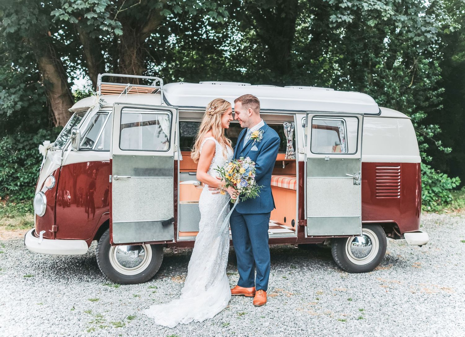 Wedding couple poses with vintage VW camper van in rustic outdoor setting.