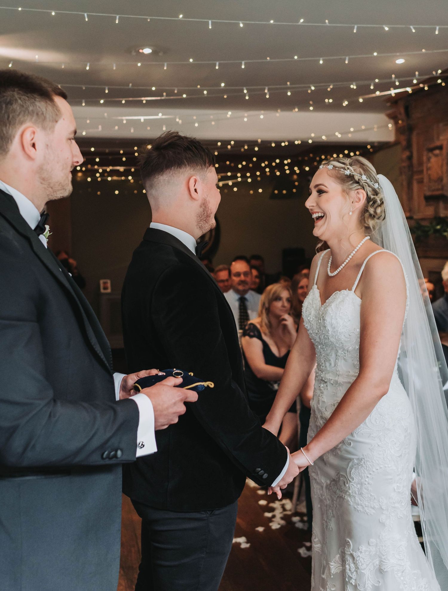 Wedding ceremony with string lights overhead and joyous laughter during vows in rustic indoor venue.