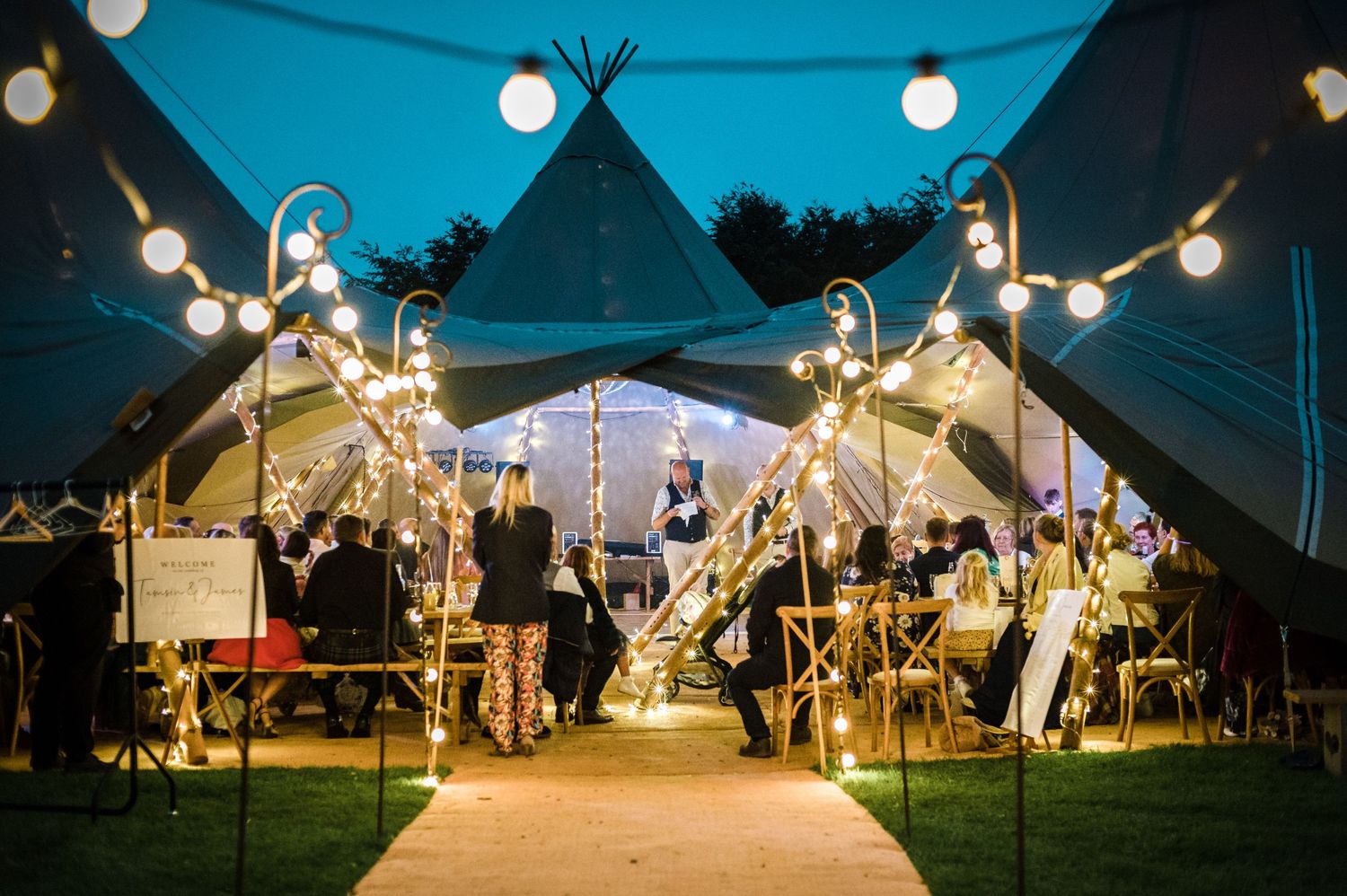Evening wedding reception setup with tipi tents and string lights creating magical atmosphere.