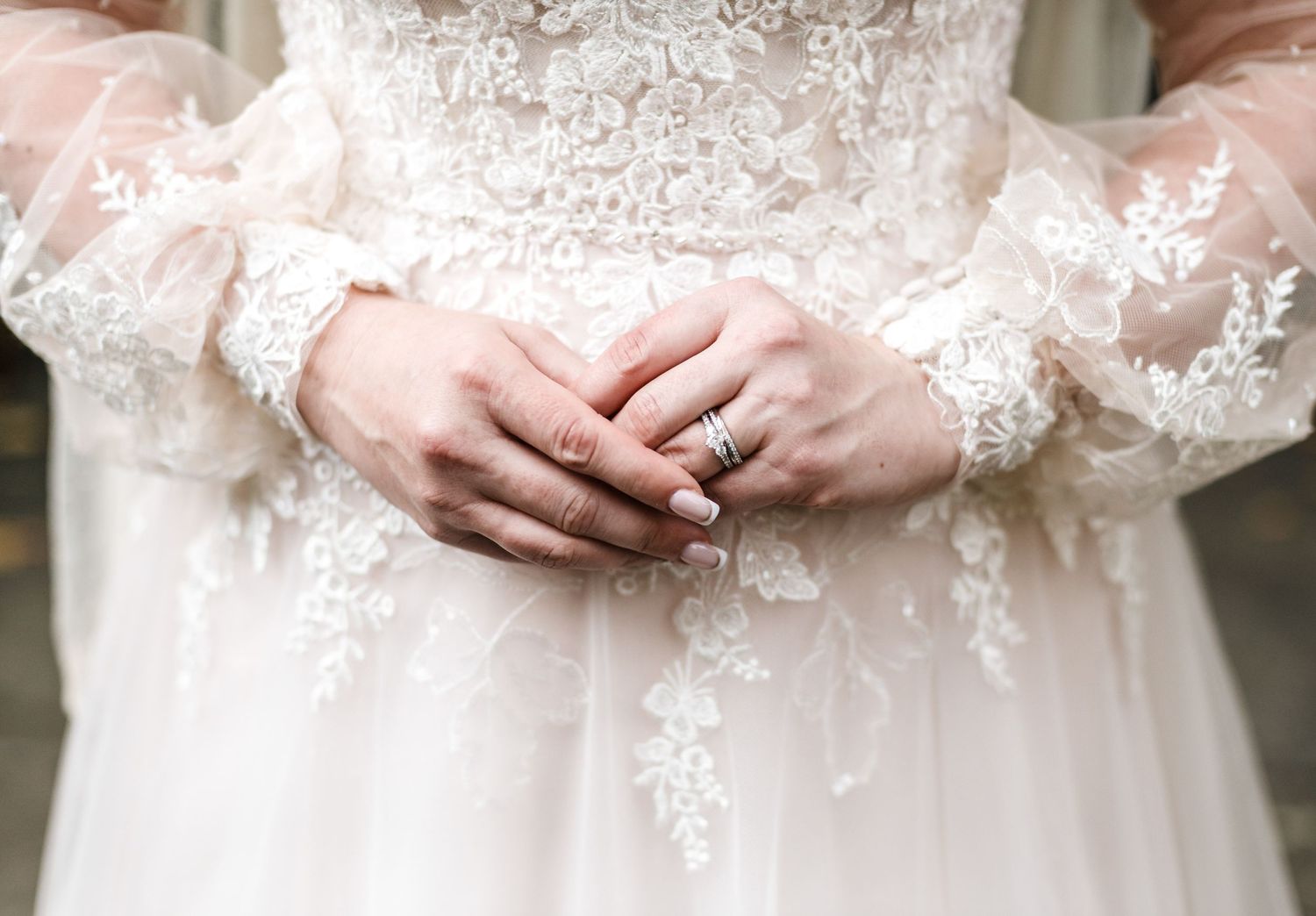 Close-up of bride's hands showing lace sleeve details and wedding ring.