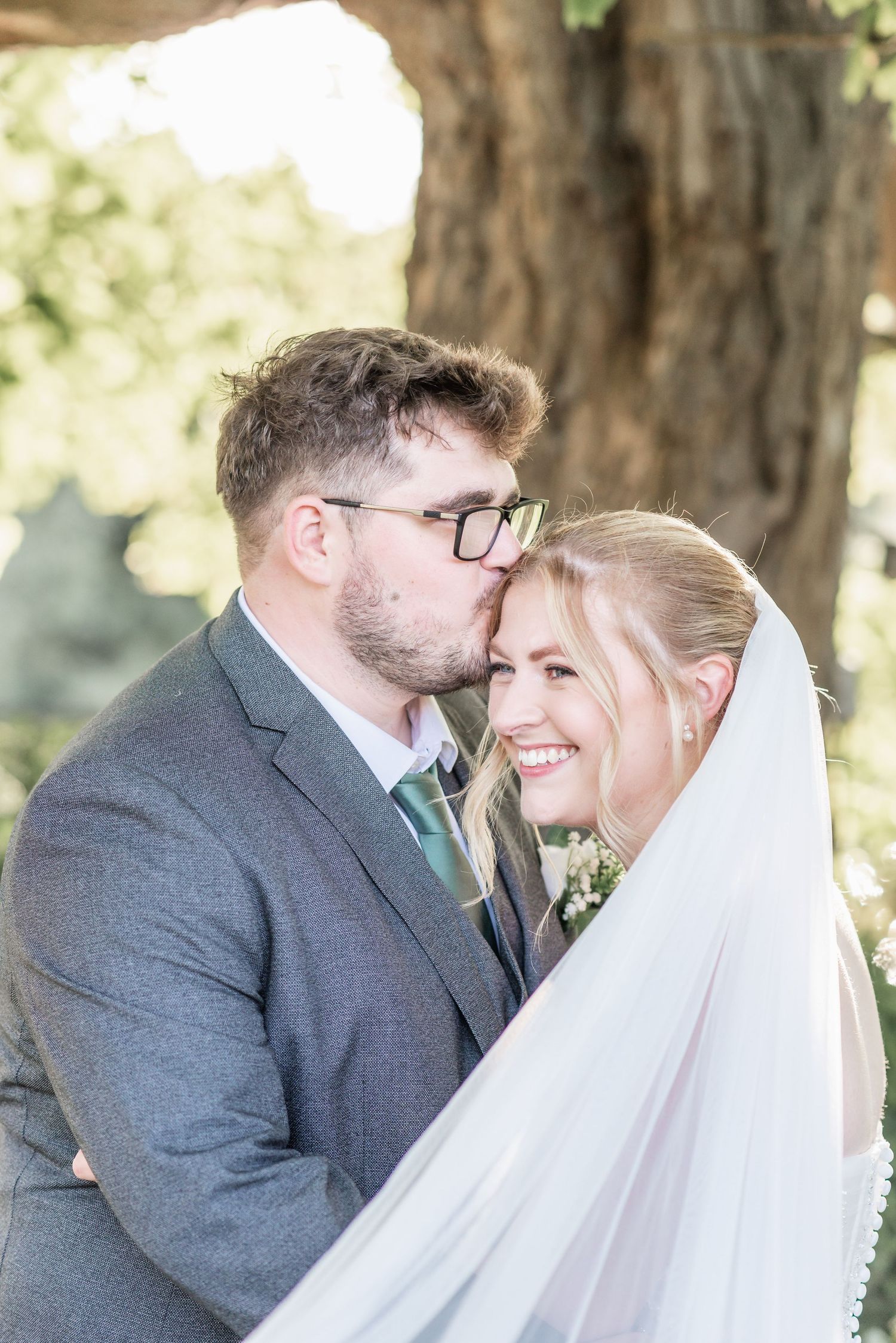 Intimate wedding portrait under trees with flowing white veil.