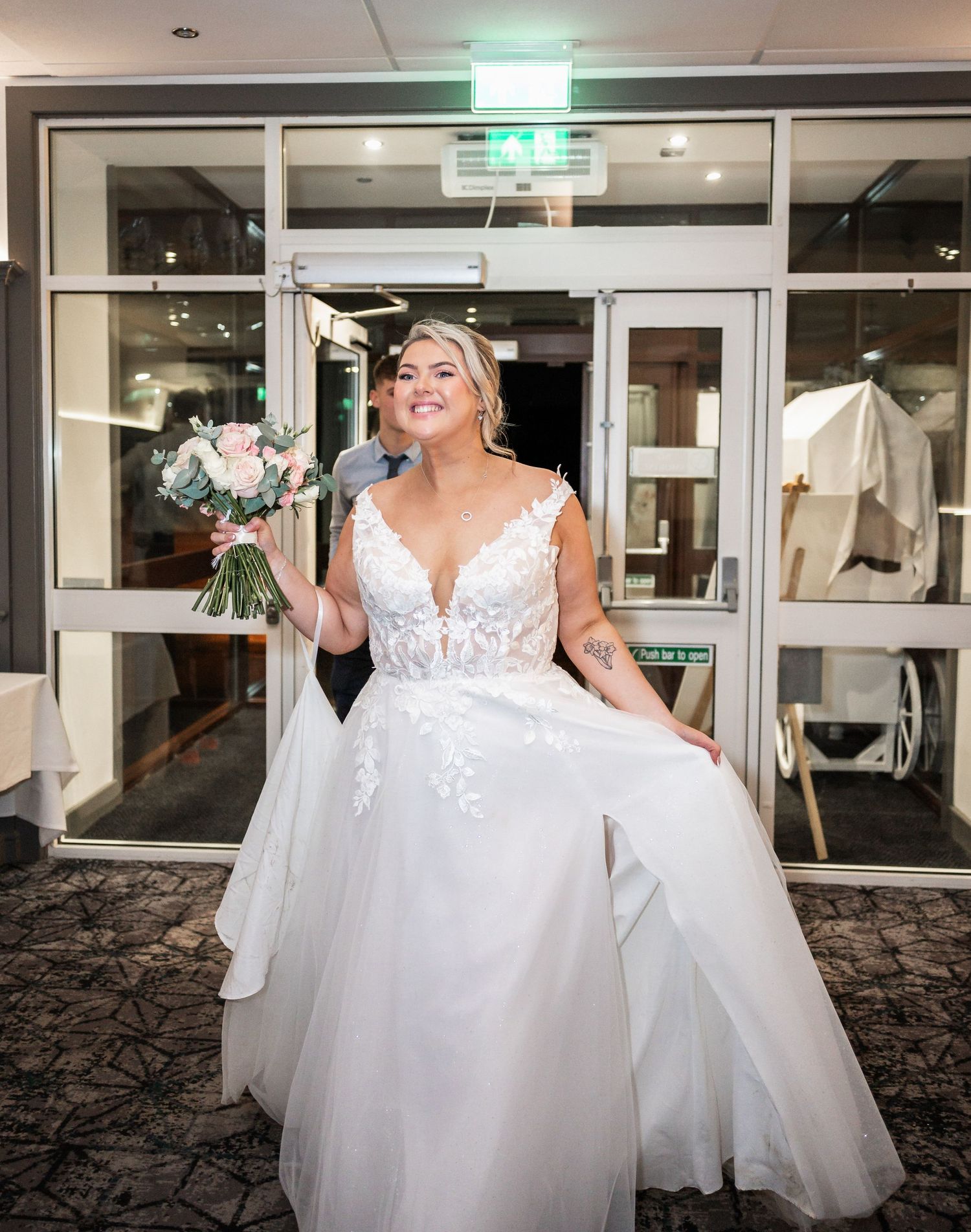 Bride in a white lace ball gown poses confidently in an elegant venue hallway.