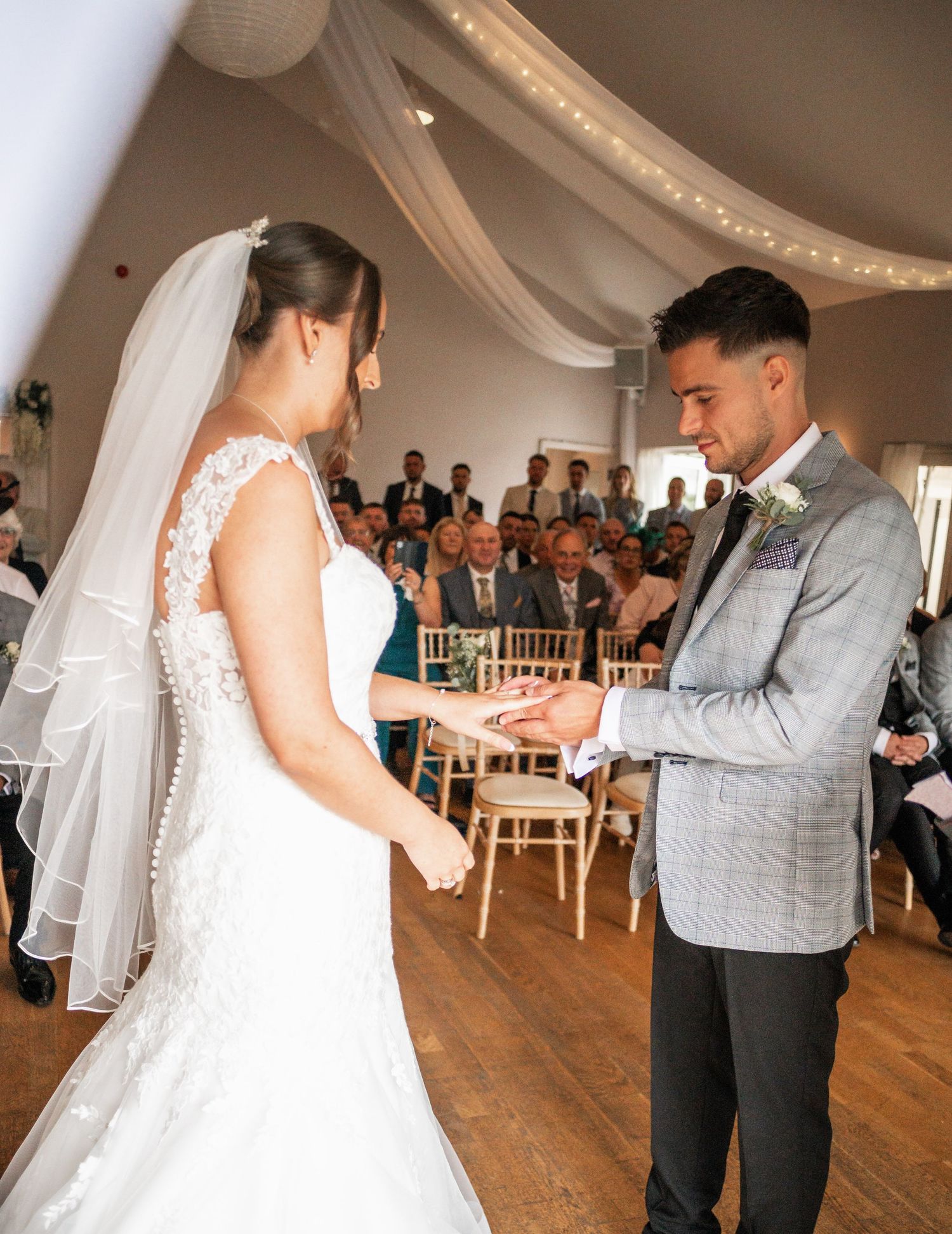 A wedding ceremony in progress inside a decorated room with white fabric draping and fairy lights.
