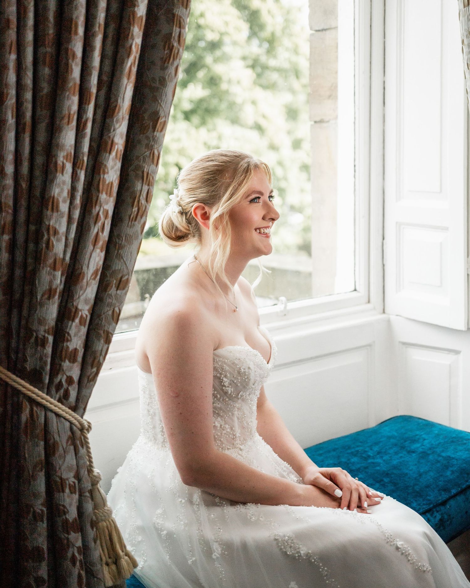 Serene bridal portrait by window with natural light illuminating white wedding gown.
