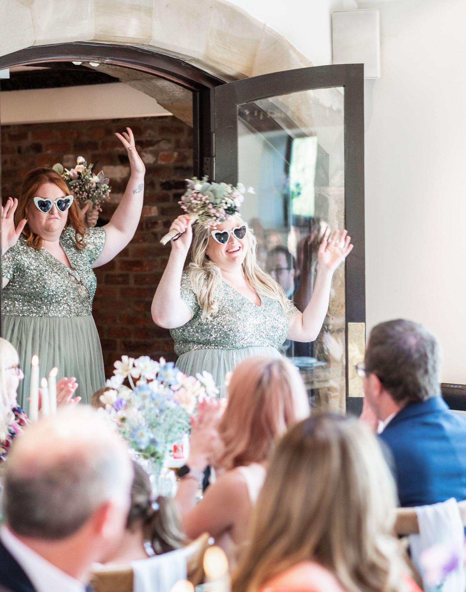 Bridesmaids in mint green dresses raise their hands in celebration during wedding reception speeches.