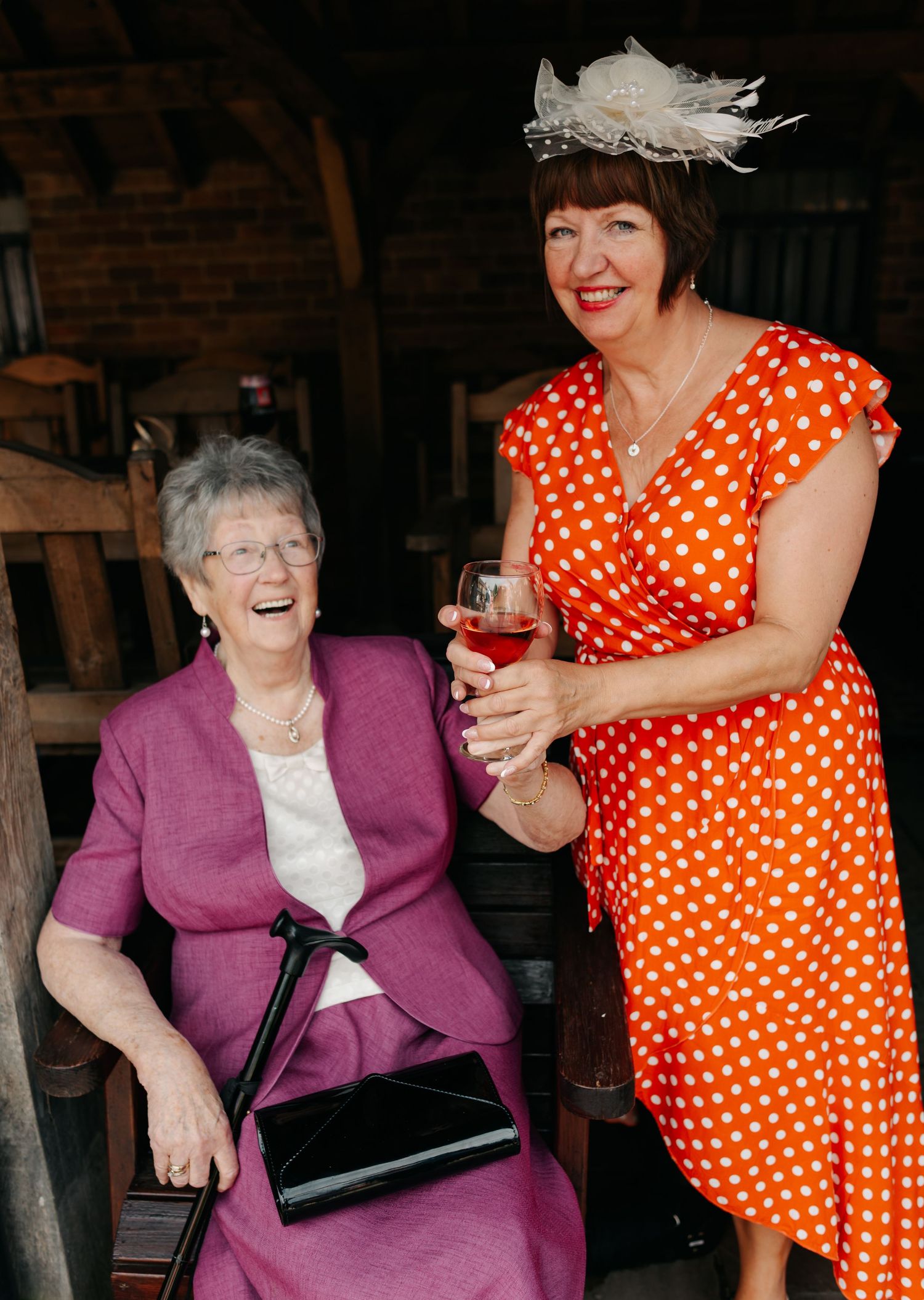 Woman in orange polka dot dress interacts playfully with another in purple sweater at social gathering.
