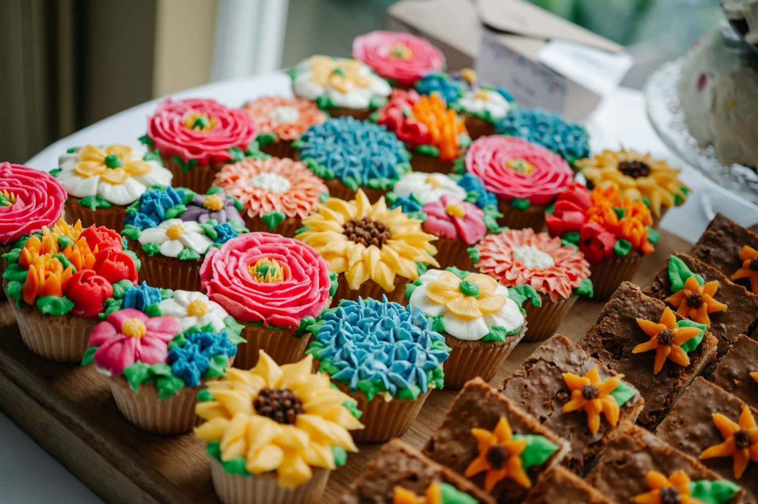 Colorful cupcakes decorated with flower designs in vibrant shades of pink, yellow, and blue.