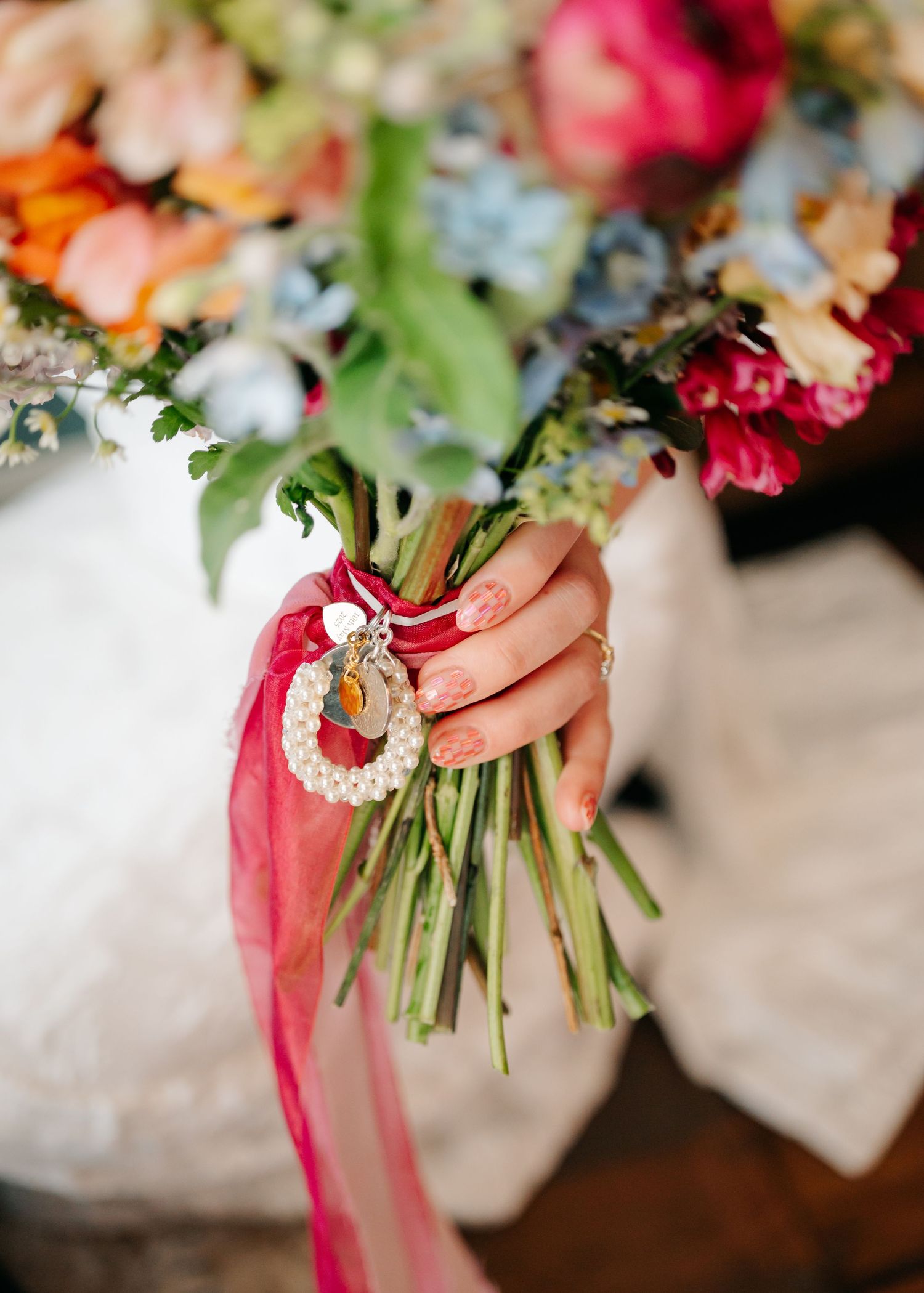 Wedding bouquet detail showing pink ribbons tied around fresh flowers and greenery.