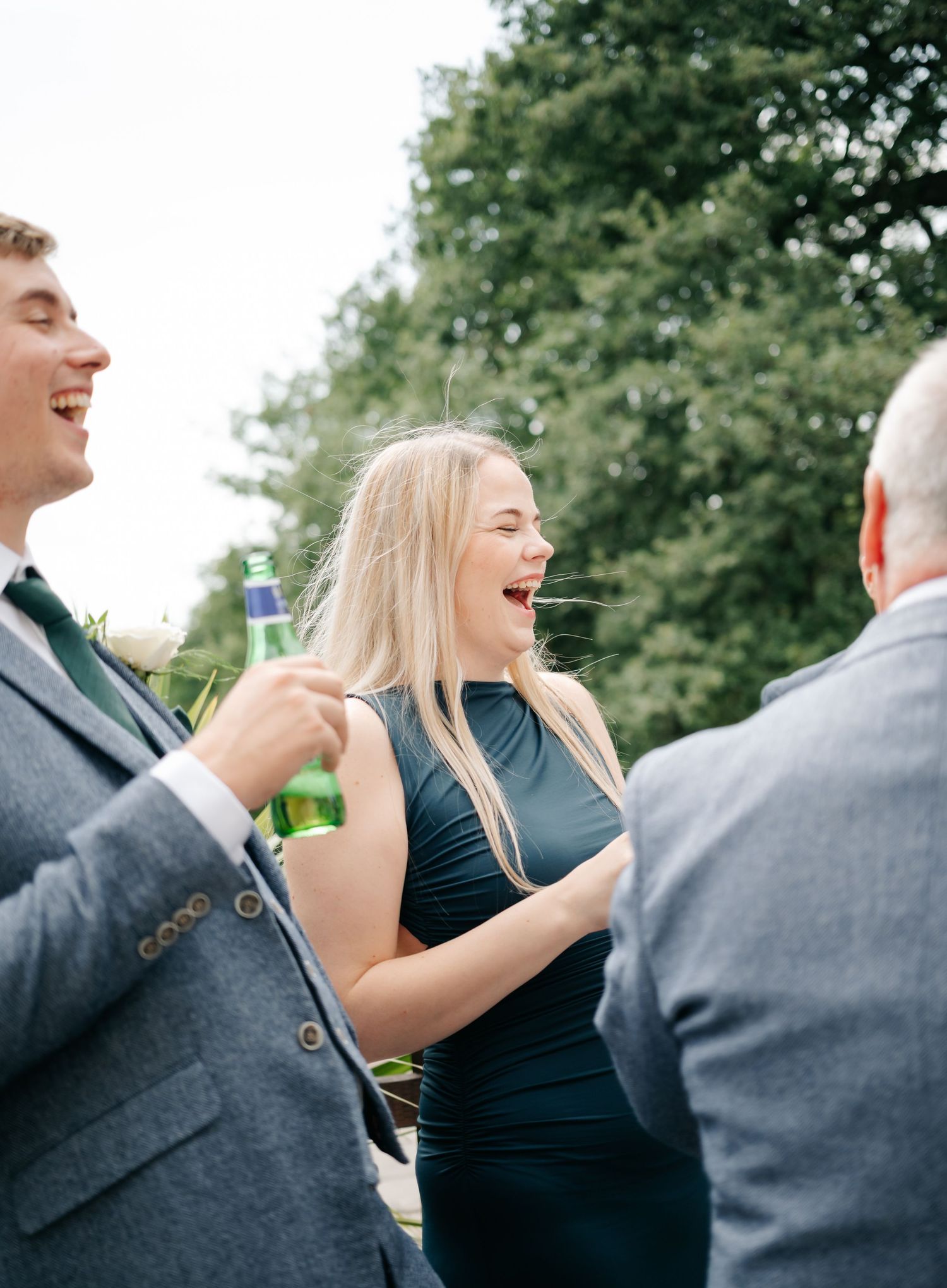 Wedding guests enjoying drinks and laughter at an outdoor reception.