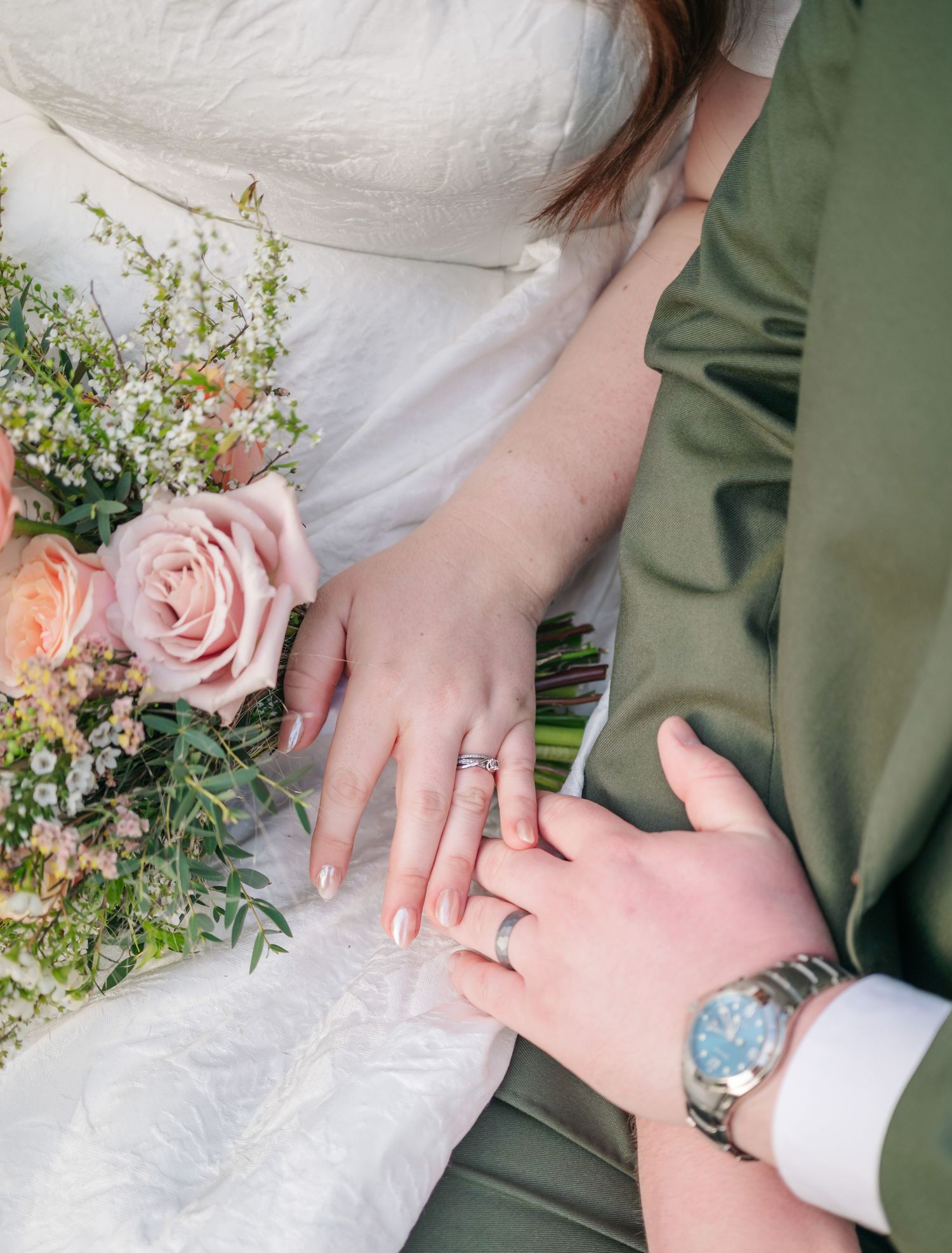 Close up of wedding rings and hands with pink rose bouquet and greenery.