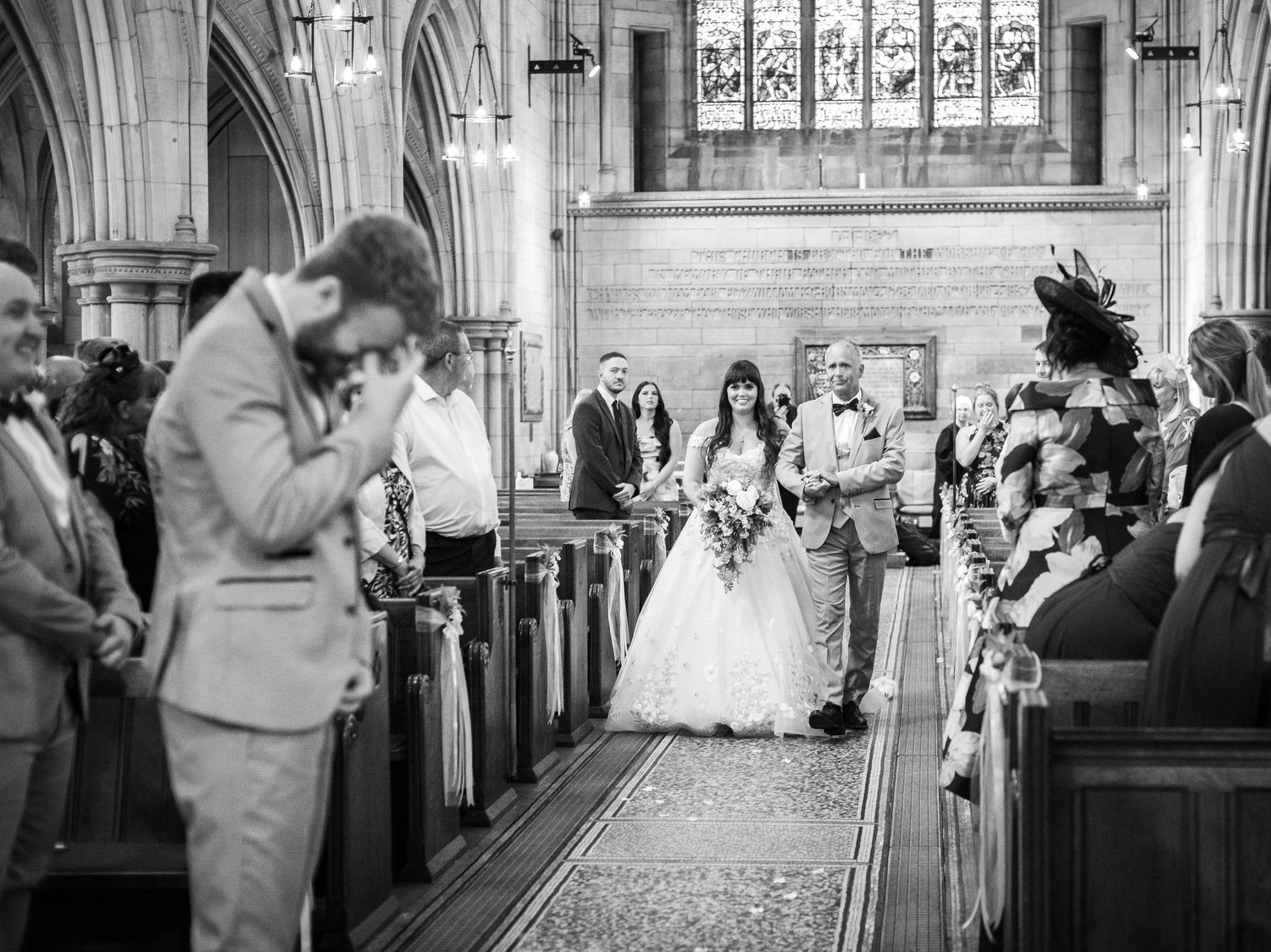 Members of a wedding party process down the aisle of a grand cathedral with ornate stone archways and pillars.