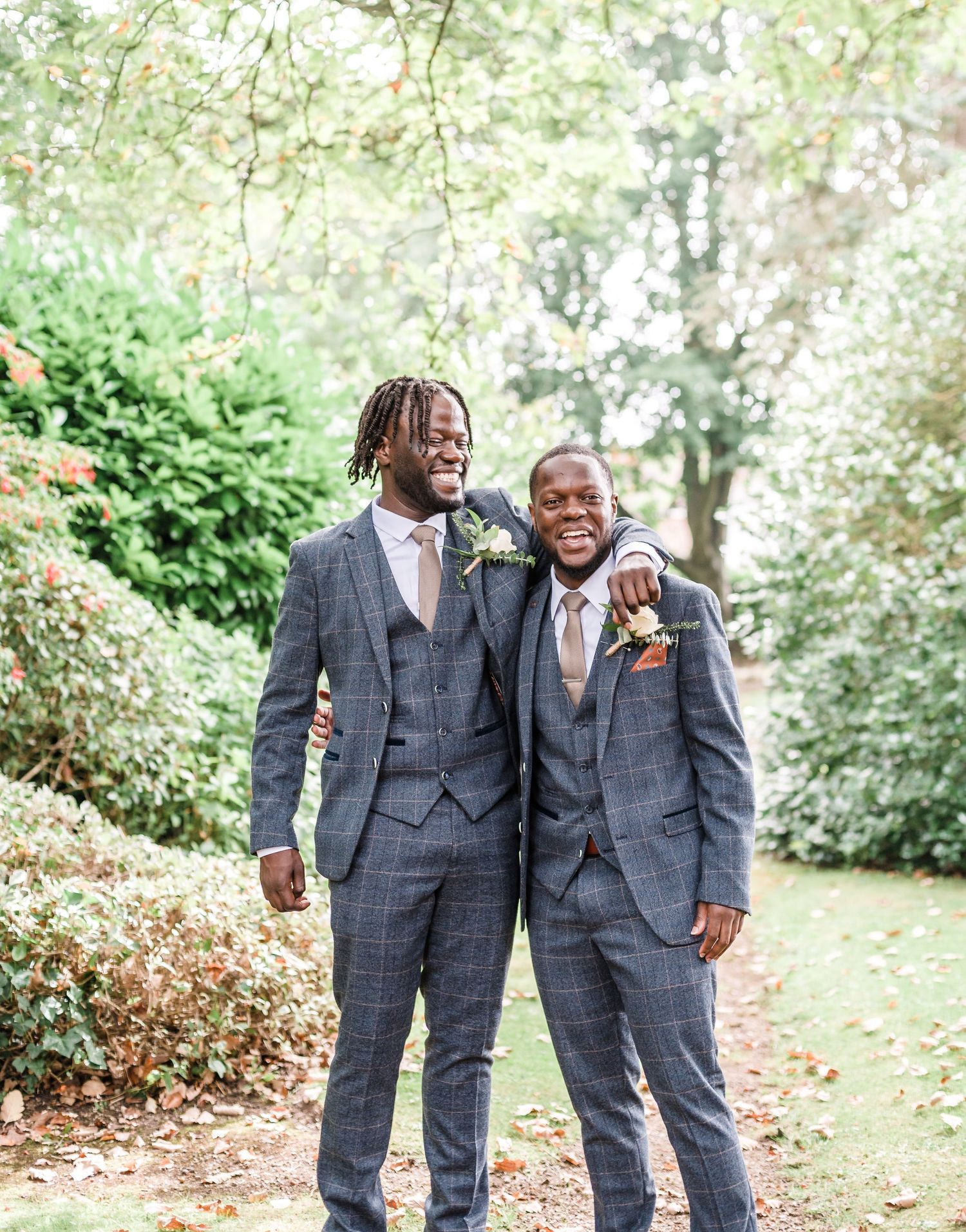 Groomsmen in matching gray plaid suits smiling together in a garden setting.