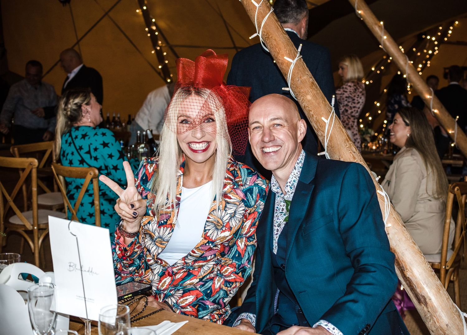 Wedding guests in colorful attire celebrating at a reception under a decorated tent.