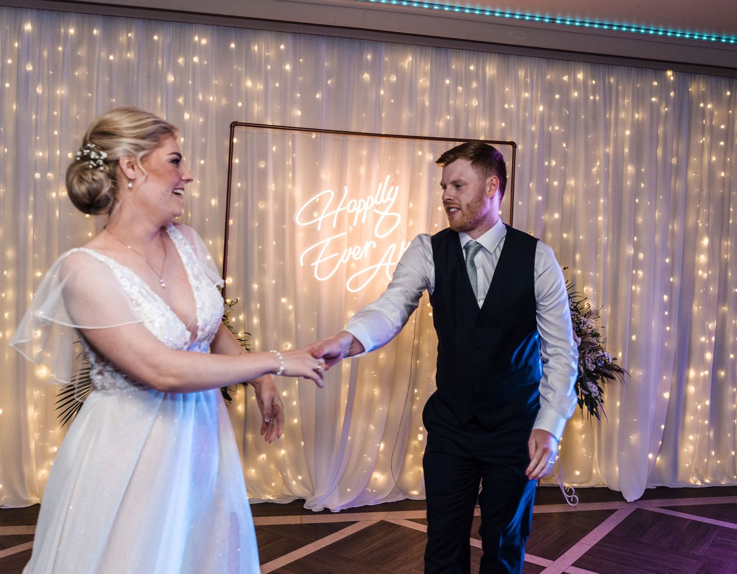 A couple shares a joyful moment during their wedding reception with twinkle lights in the background.