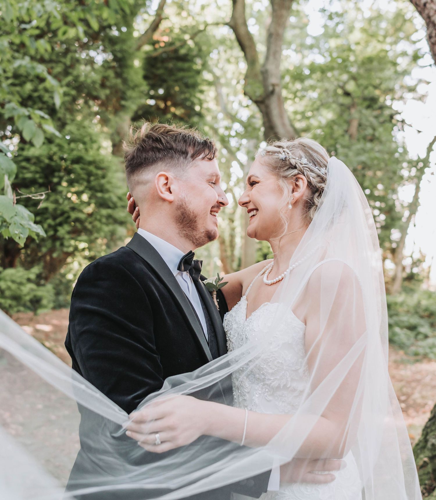 Candid moment of laughter between newlyweds as bride's veil catches the breeze.