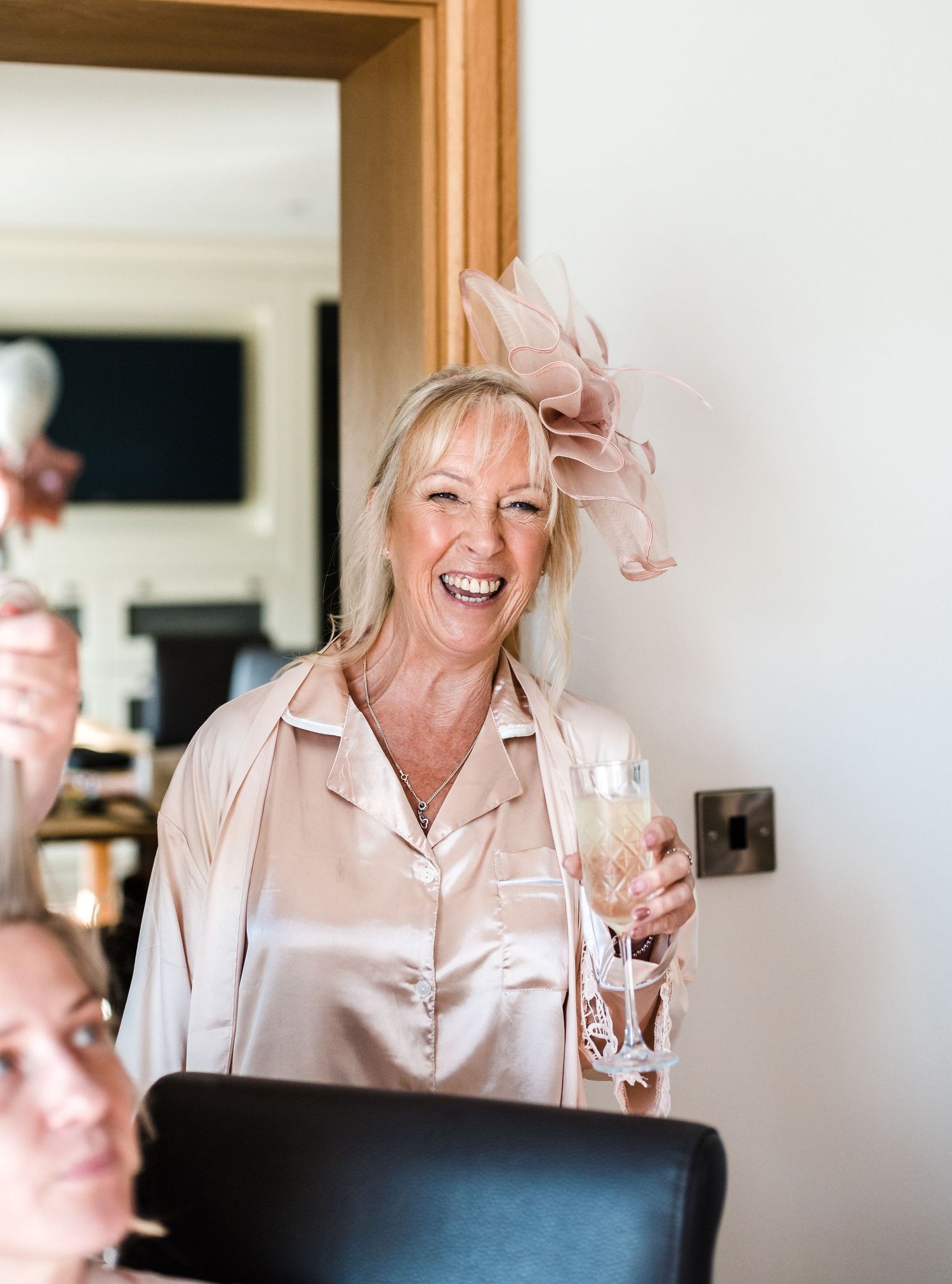Wedding guest in pink satin pajamas laughing while holding champagne glass at celebration.