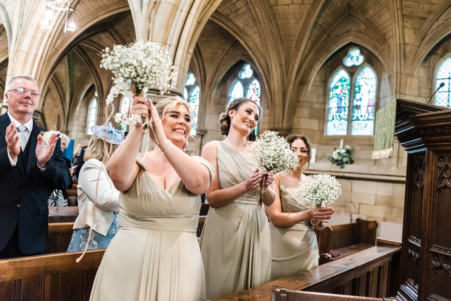 Wedding guests and bridal party celebrate with applause inside a historic church with vaulted ceilings.