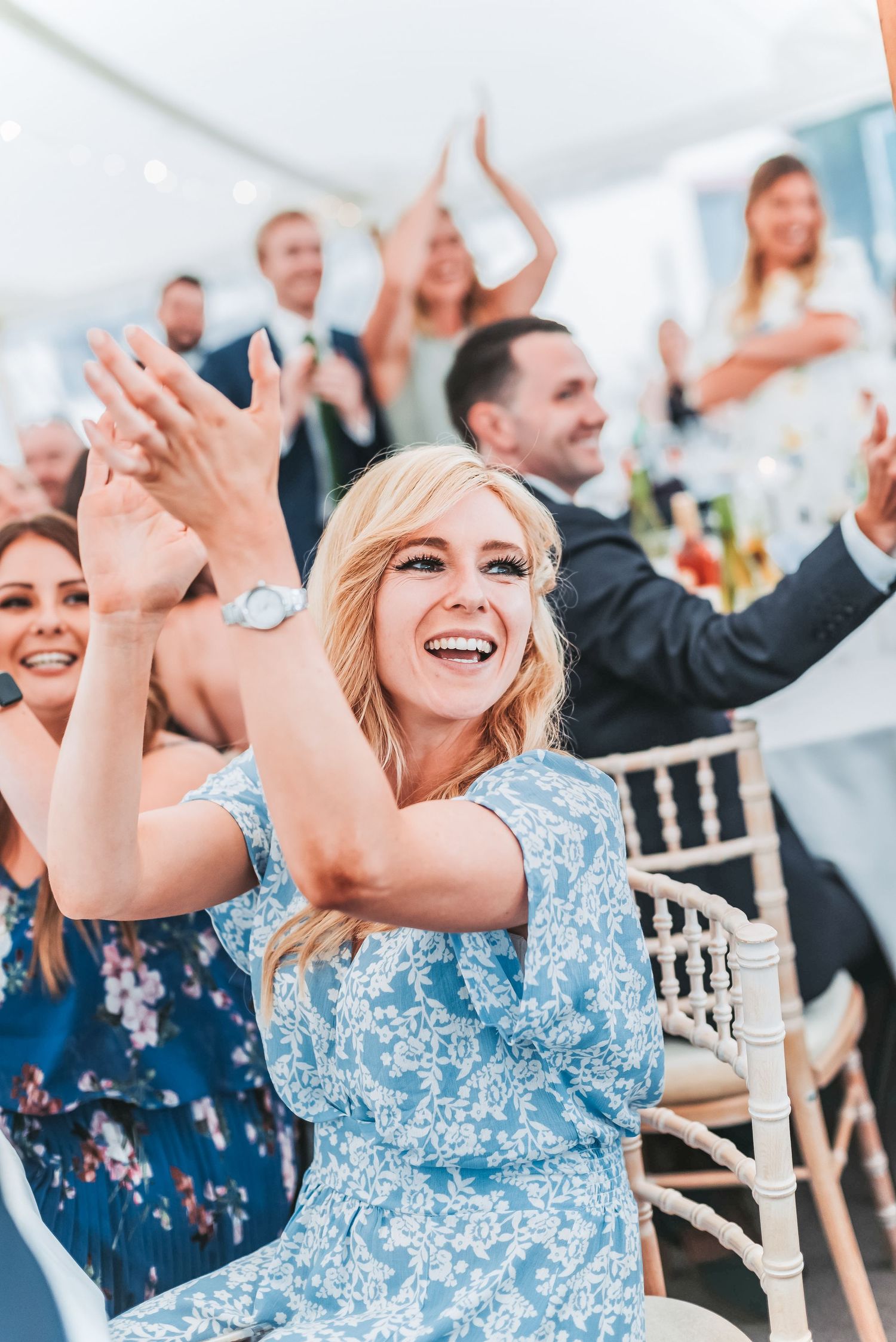 Guests clapping and celebrating during wedding reception under white tent with elegant decor.