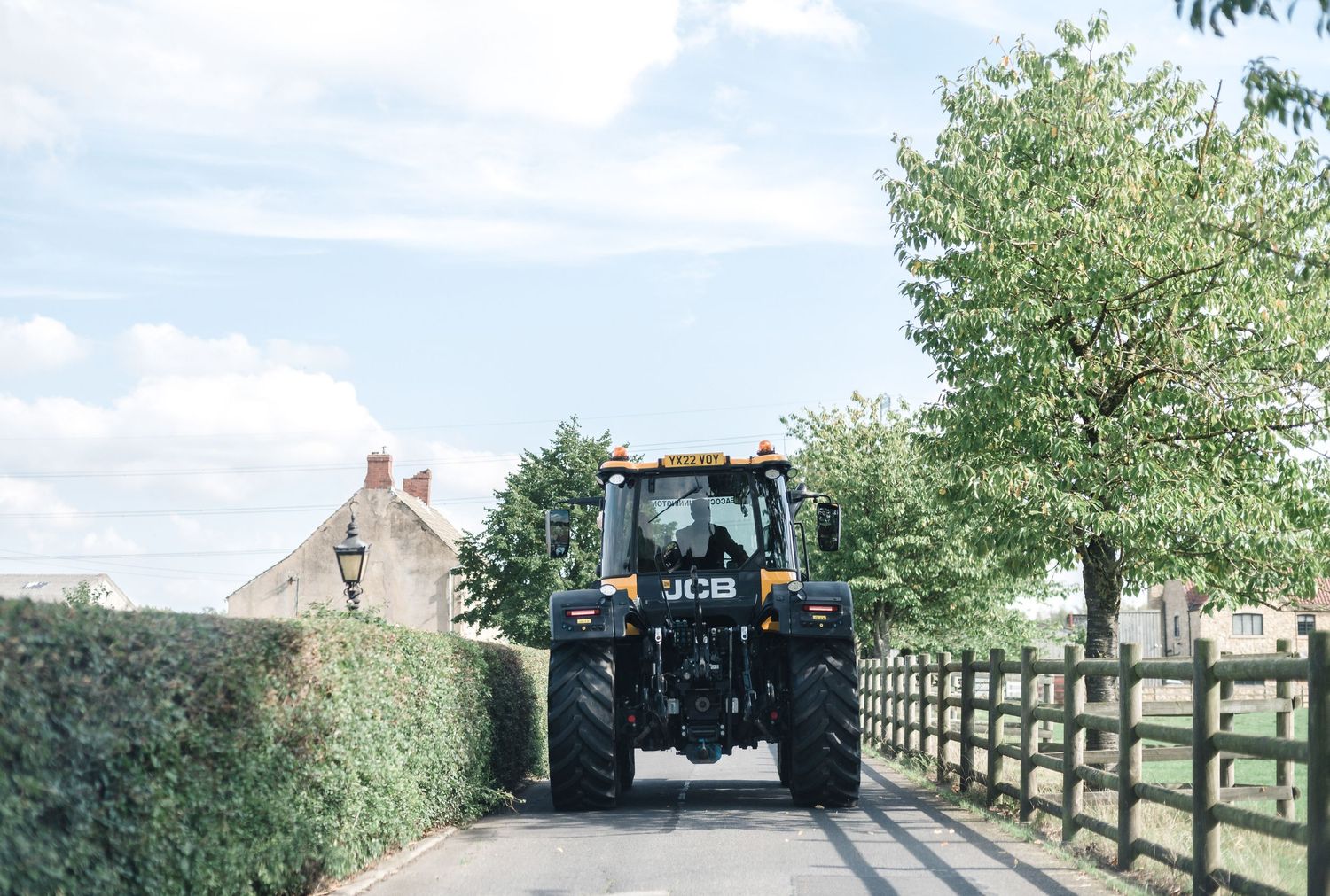 Yellow tractor driving down country lane with hedgerows.