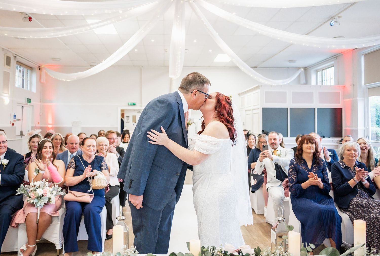 Wedding celebration moment in a white decorated venue with guests applauding.
