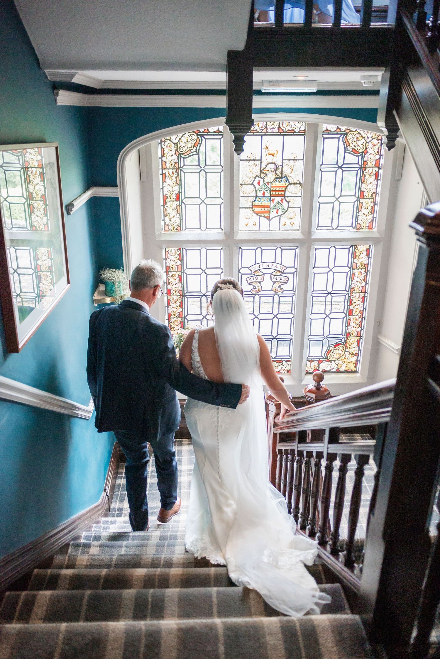A couple descends a staircase with beautiful stained glass windows in the background.