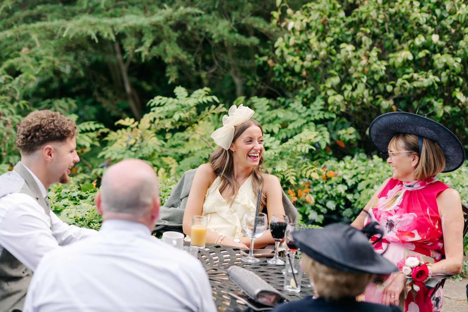 Wedding guests toast and celebrate at an outdoor garden reception table surrounded by lush greenery.