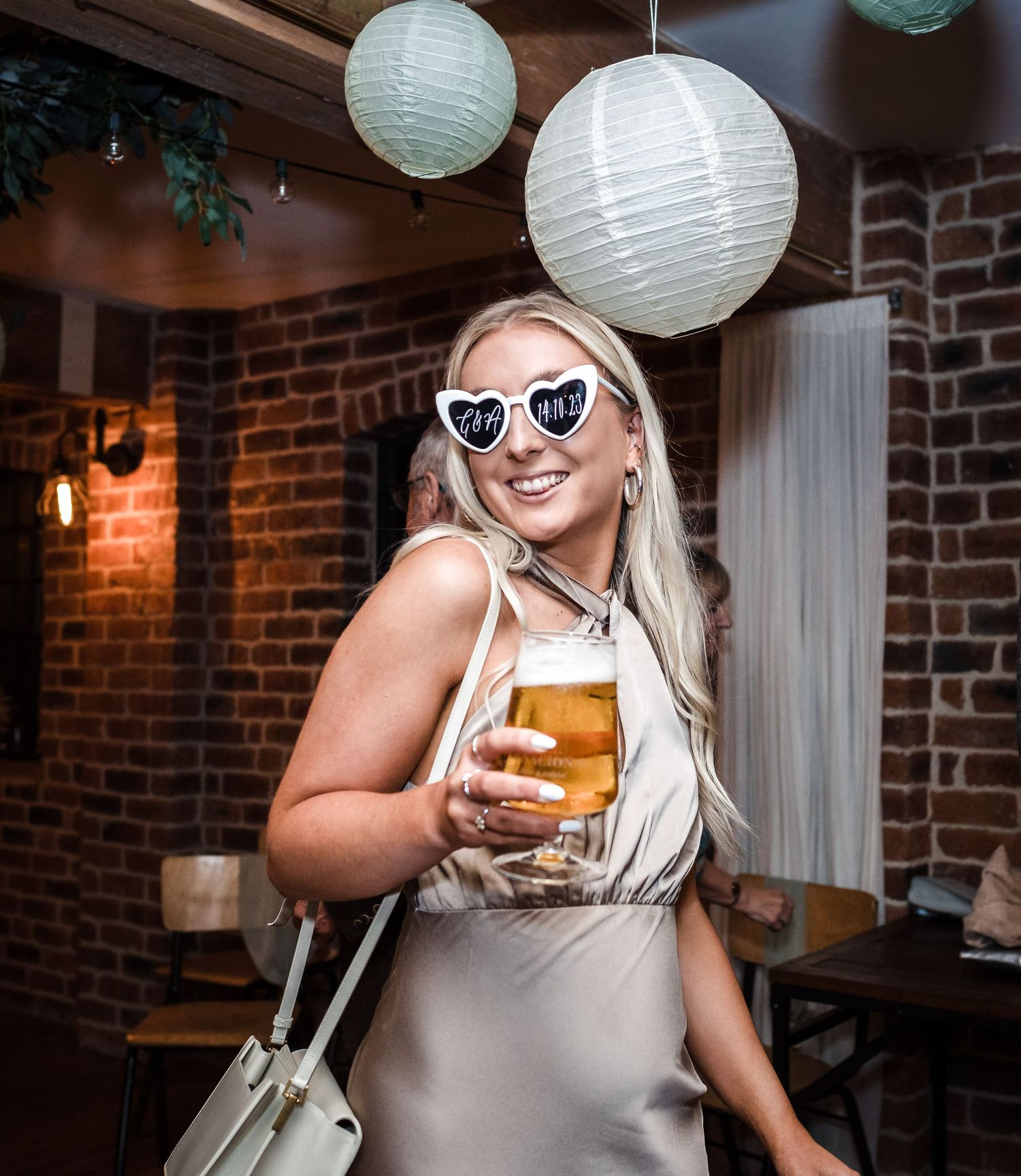 Guest in heart-shaped sunglasses holding a beer at rustic wedding reception.
