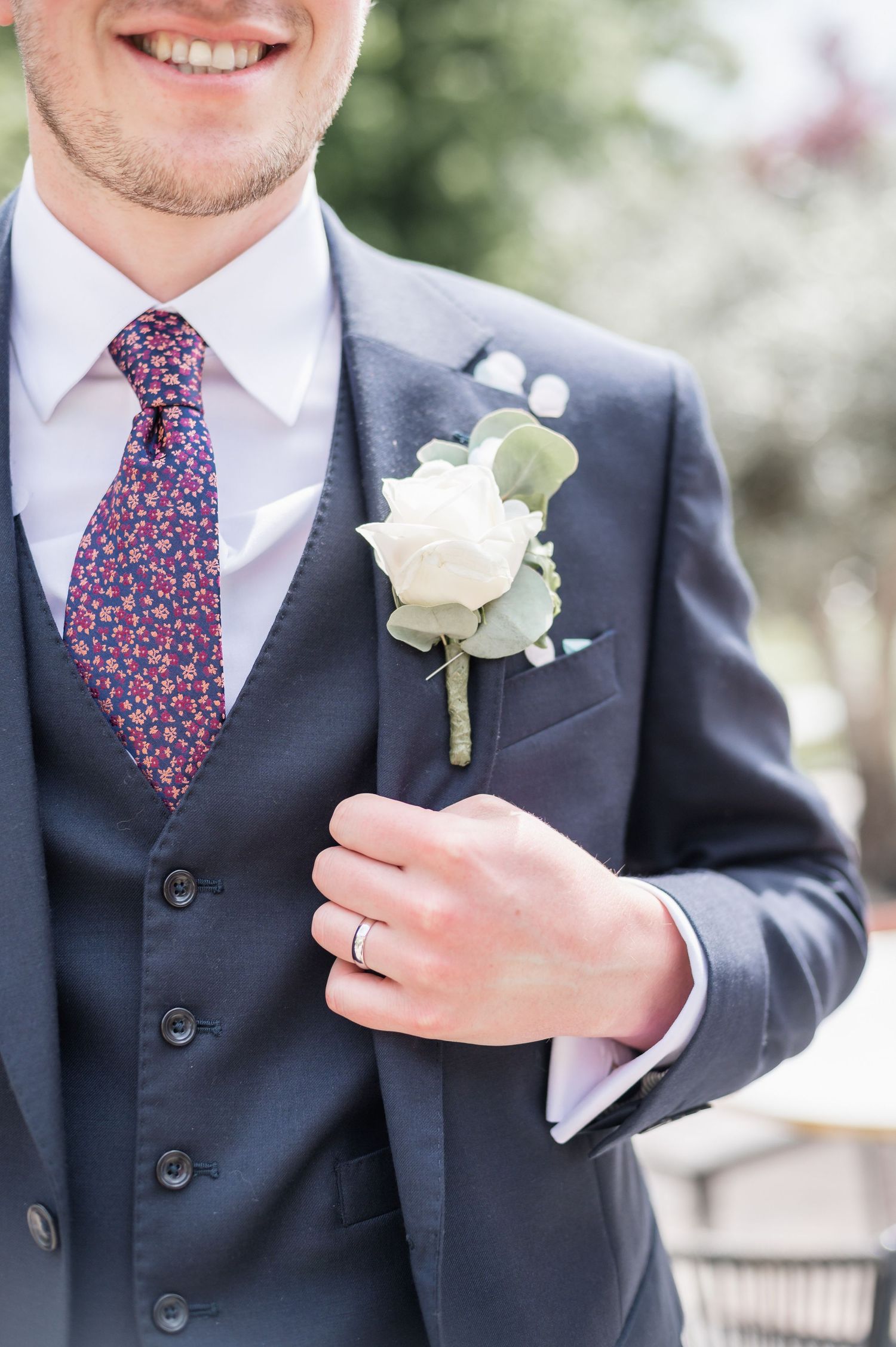 Groom wearing navy suit with floral tie and white rose boutonniere.