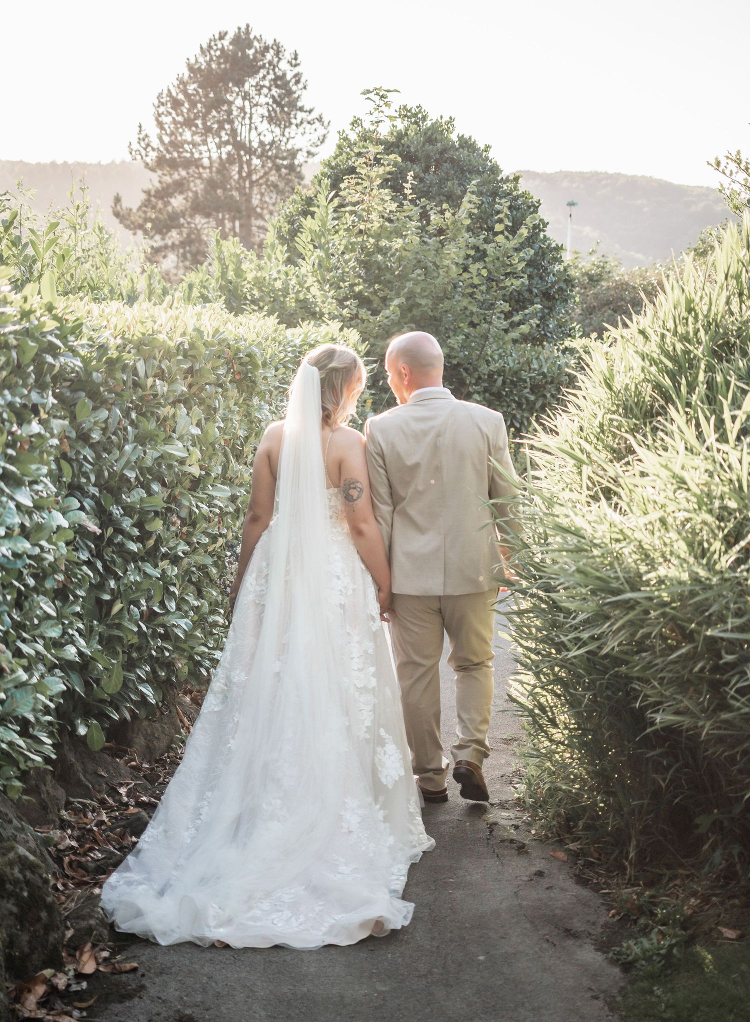 Newlyweds walking down garden path during golden hour sunset.