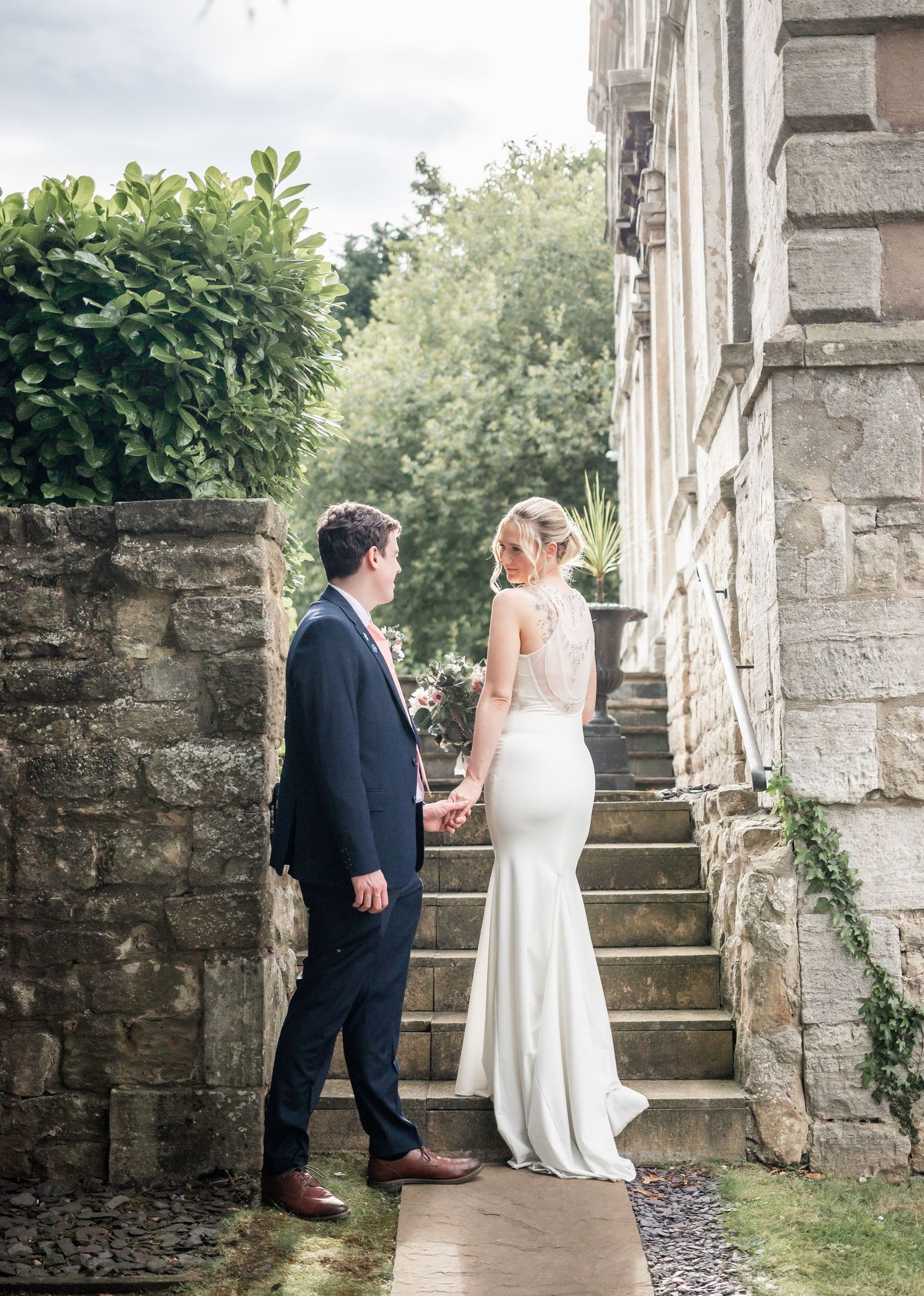 Elegant couple poses on stone staircase in formal wedding attire.