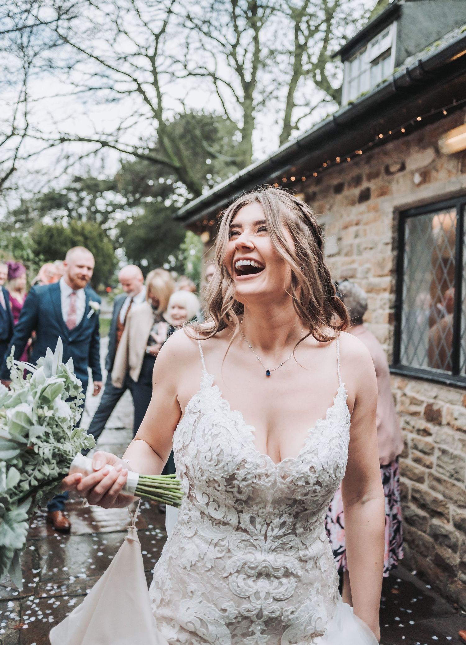 Candid outdoor wedding moment with natural stone backdrop and string lights.