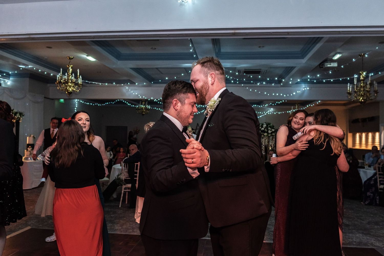 Couples slow dancing at wedding reception in dimly lit ballroom.