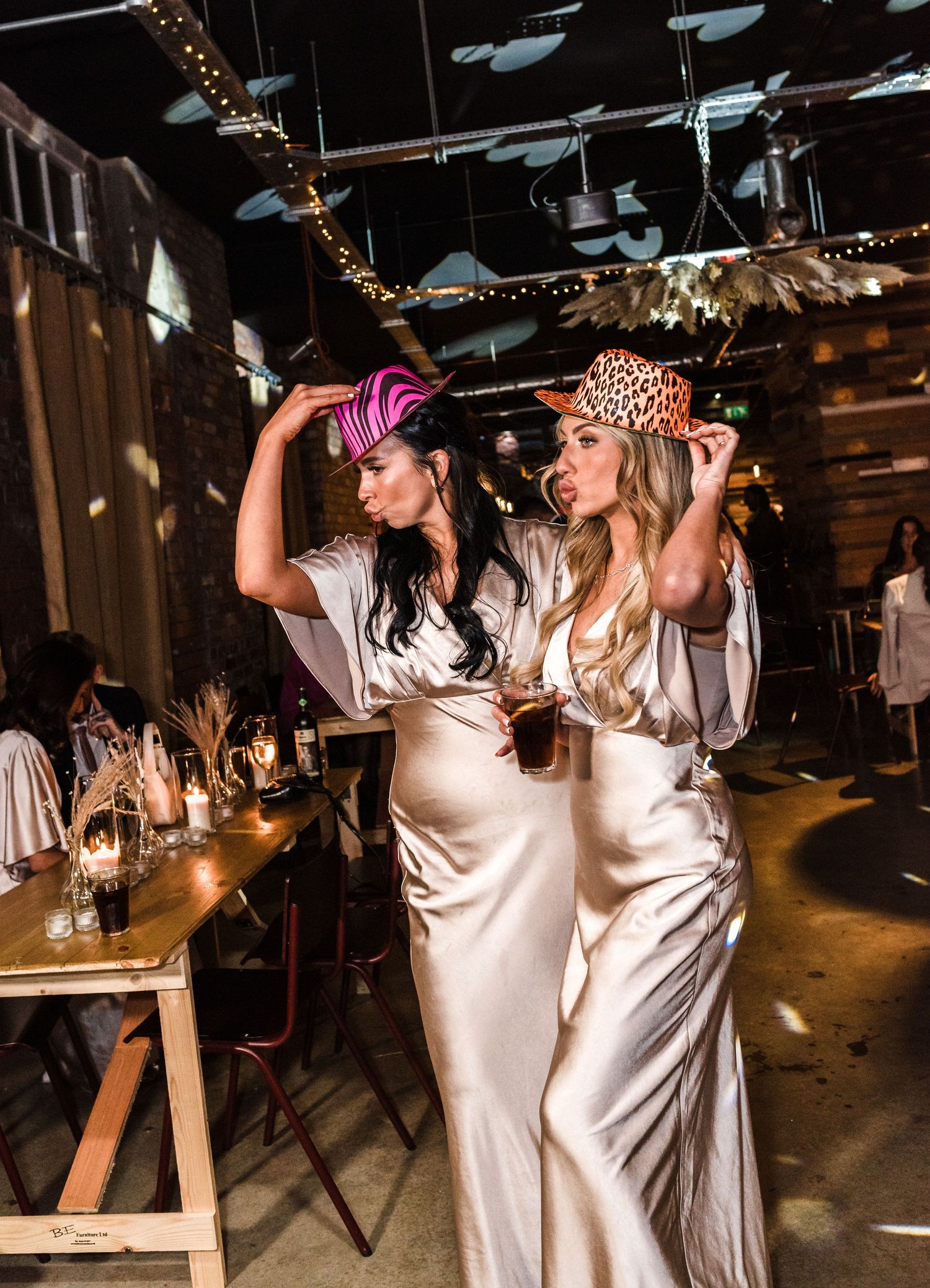 Two women in silk dresses and colorful headpieces pose at a wedding reception.