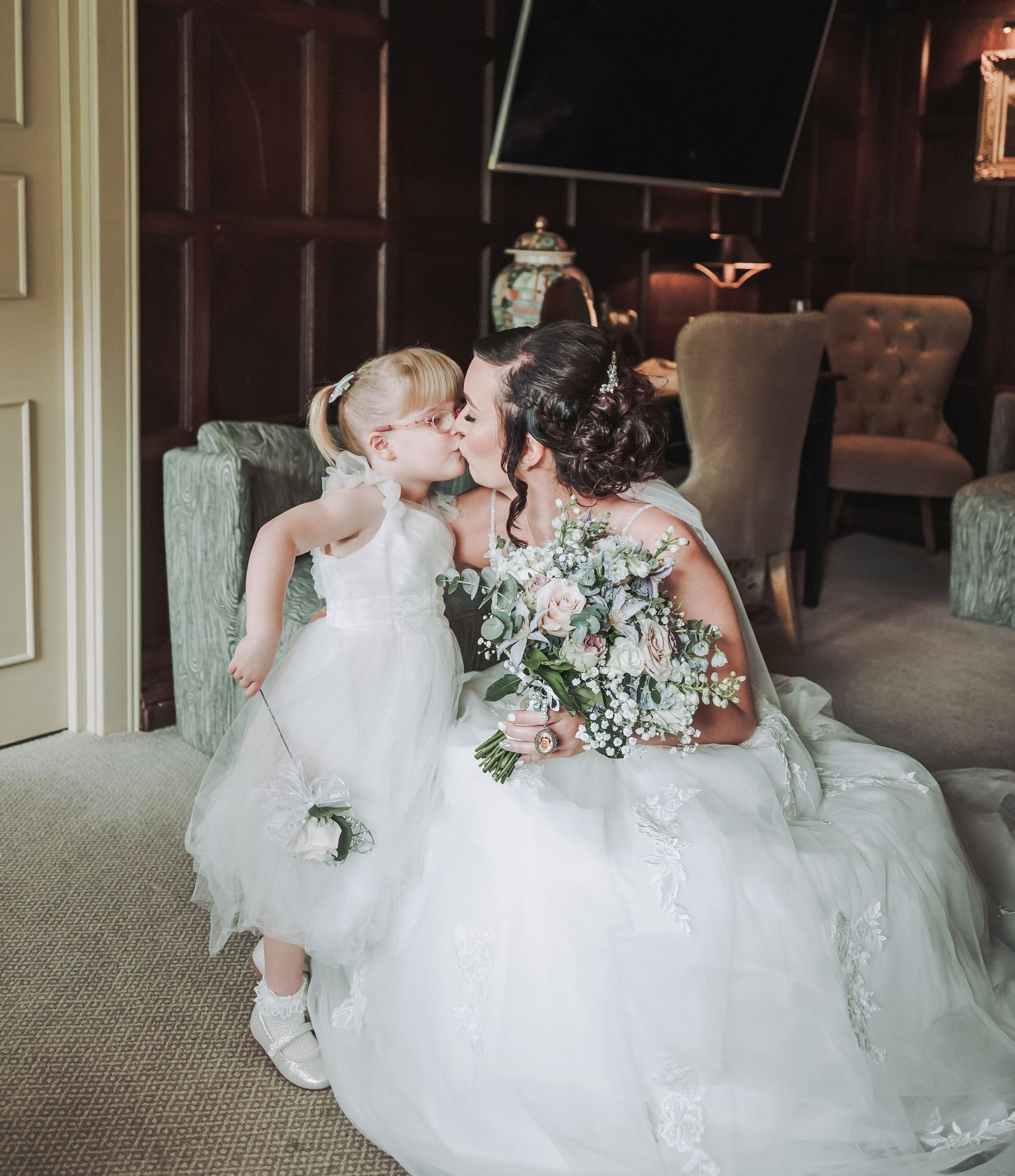 Sweet moment shared in an elegant indoor setting with white dresses and floral bouquet.