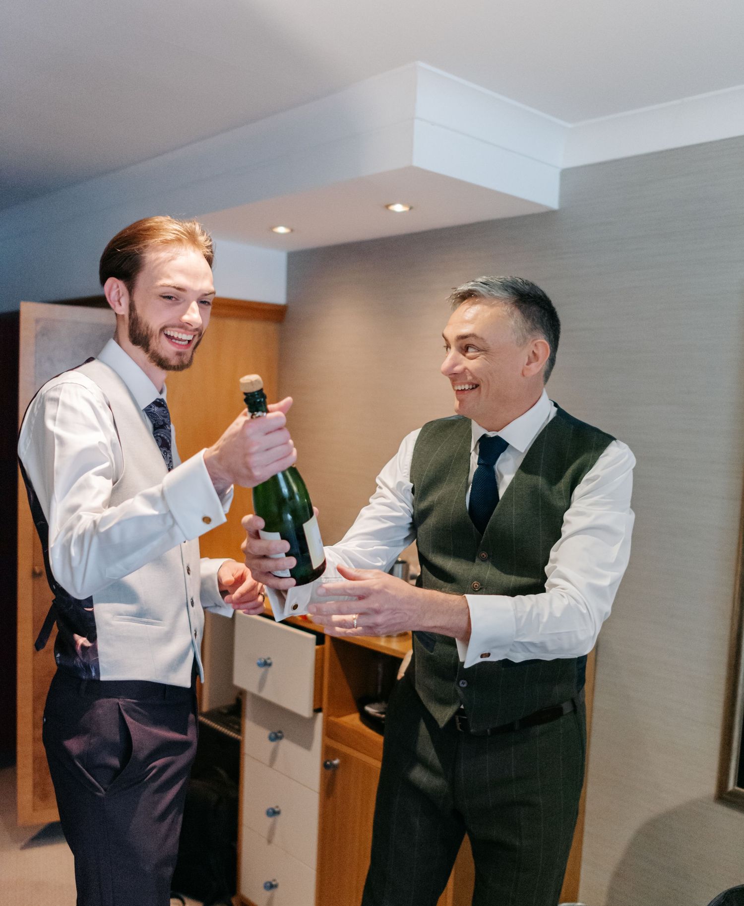 Wedding party members in formal attire sharing drinks and laughs while getting ready.