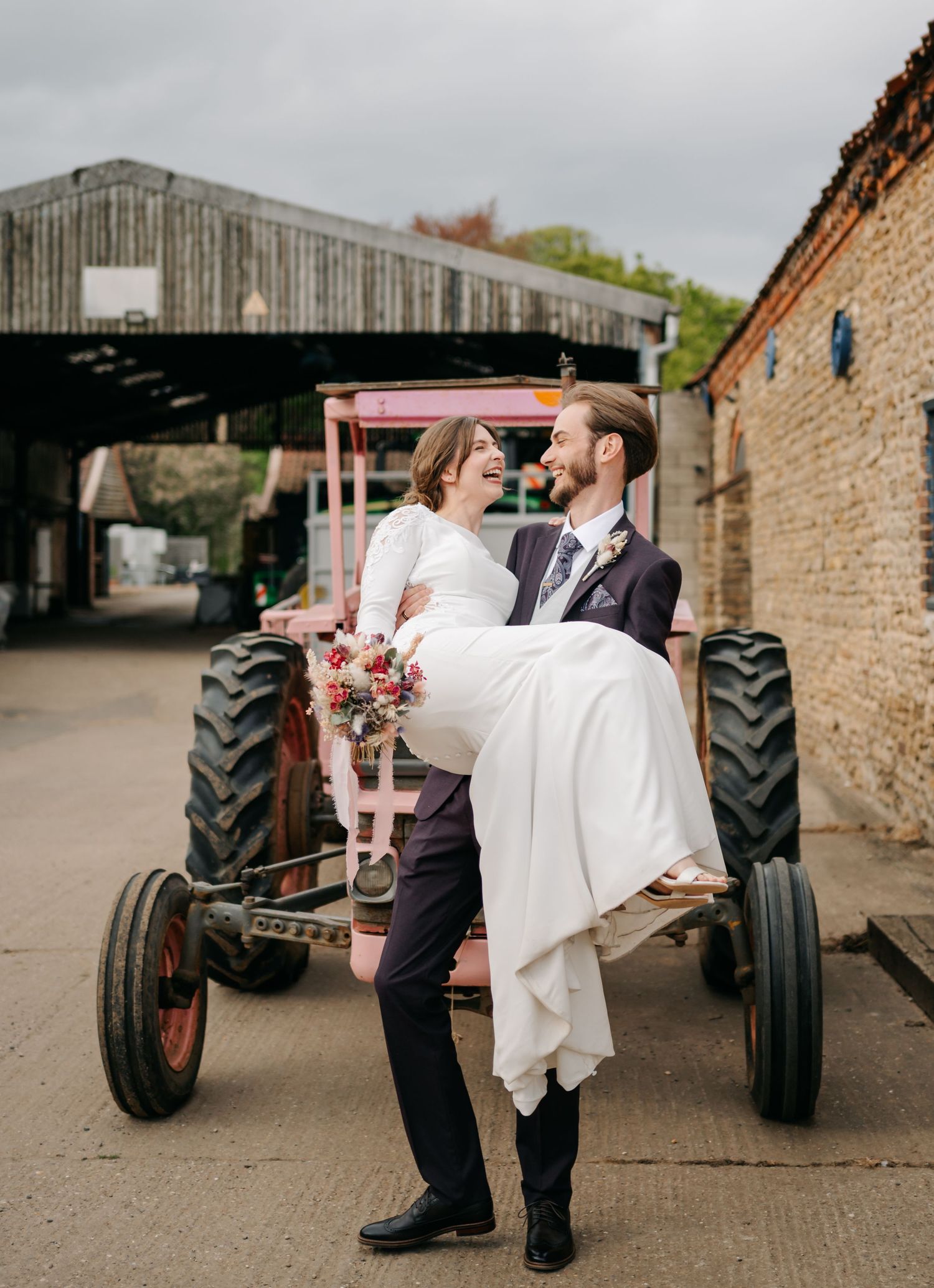 Wedding couple sharing romantic moments near vintage tractors at rustic farm venue.