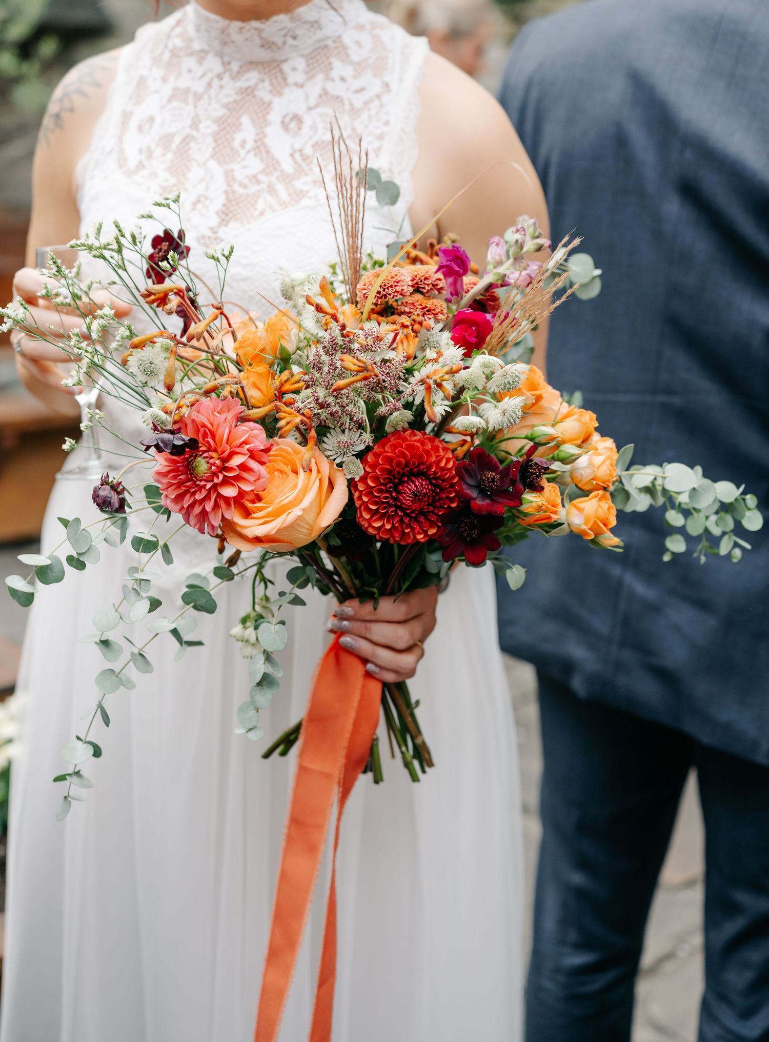Vibrant autumn wedding bouquet with orange and red flowers tied with silk ribbon.